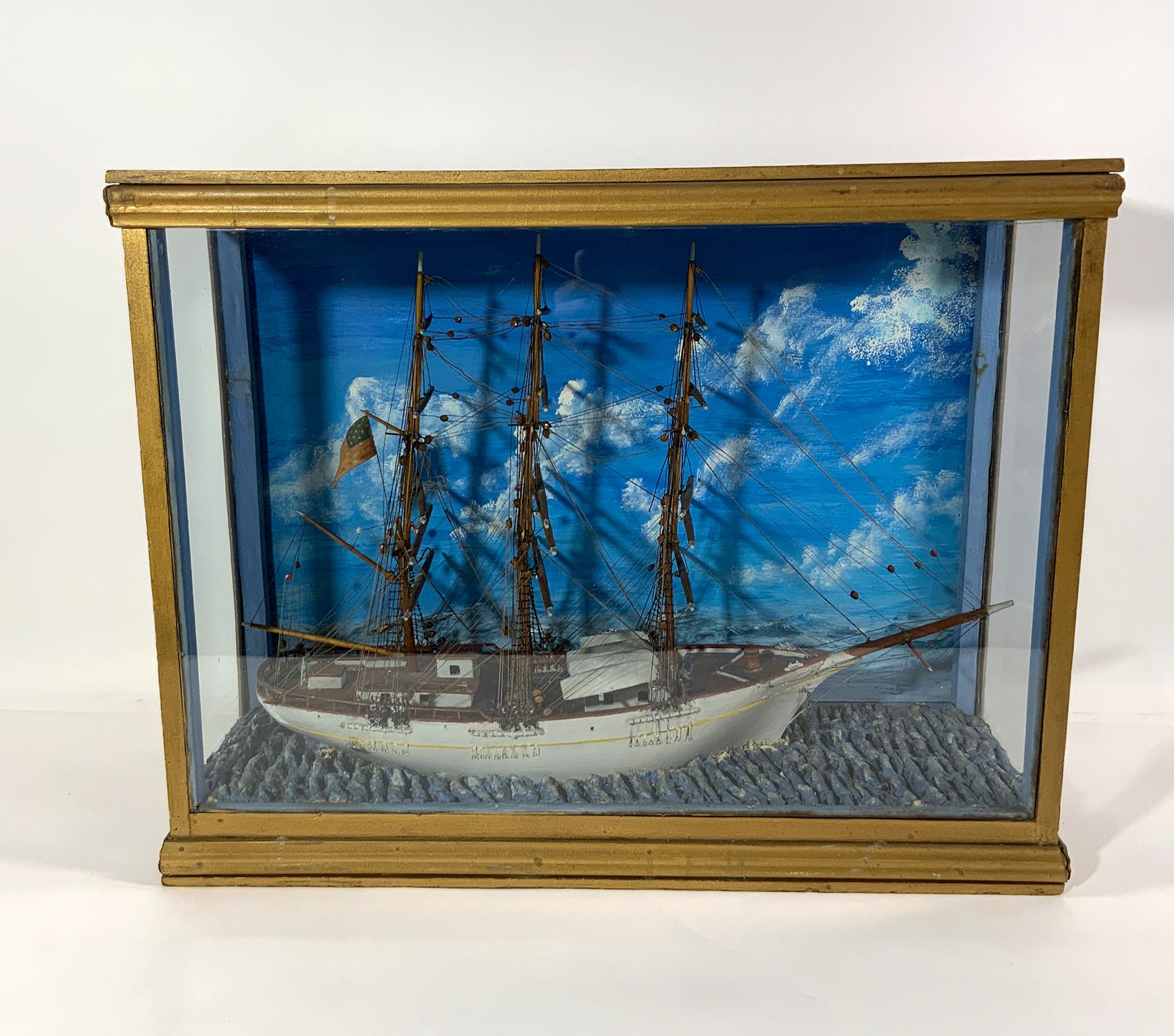 Cased diorama of a three masthead clipper ship. Fully rigged with fifteen spars on the three masts. Deck details include built up cabins, hatched, capstan, wheel house, cleats, clocks, etc.. Set into a clay sea. Painted sky background. Glass case.