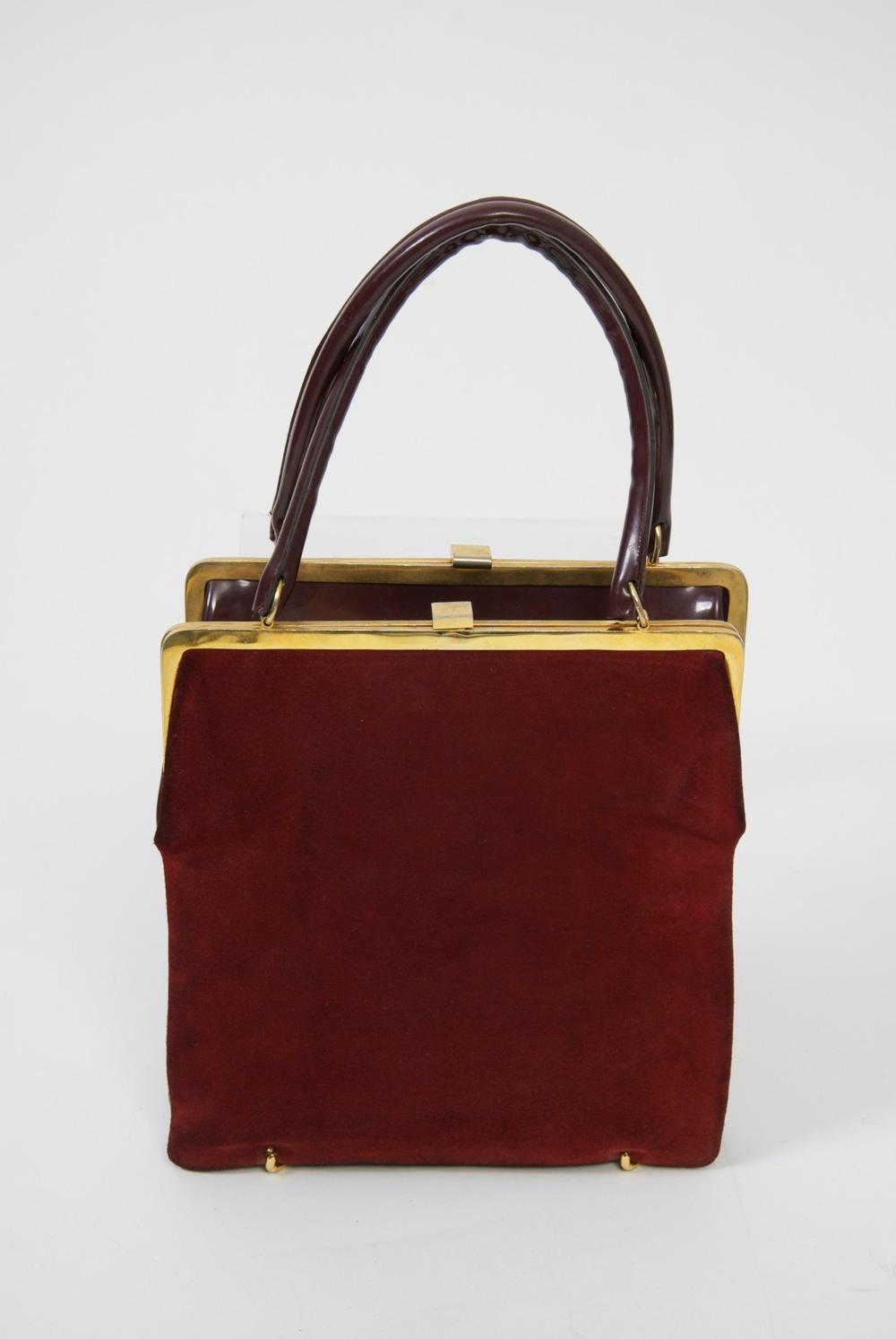 Unique, innovative design, this vintage handbag, c. 1960s, consists of two identical bags connected at bottom by goldtone rings, which allow it to reverse from wine suede to wine patent. Each has an identical gold metal frame and clasp, as well as