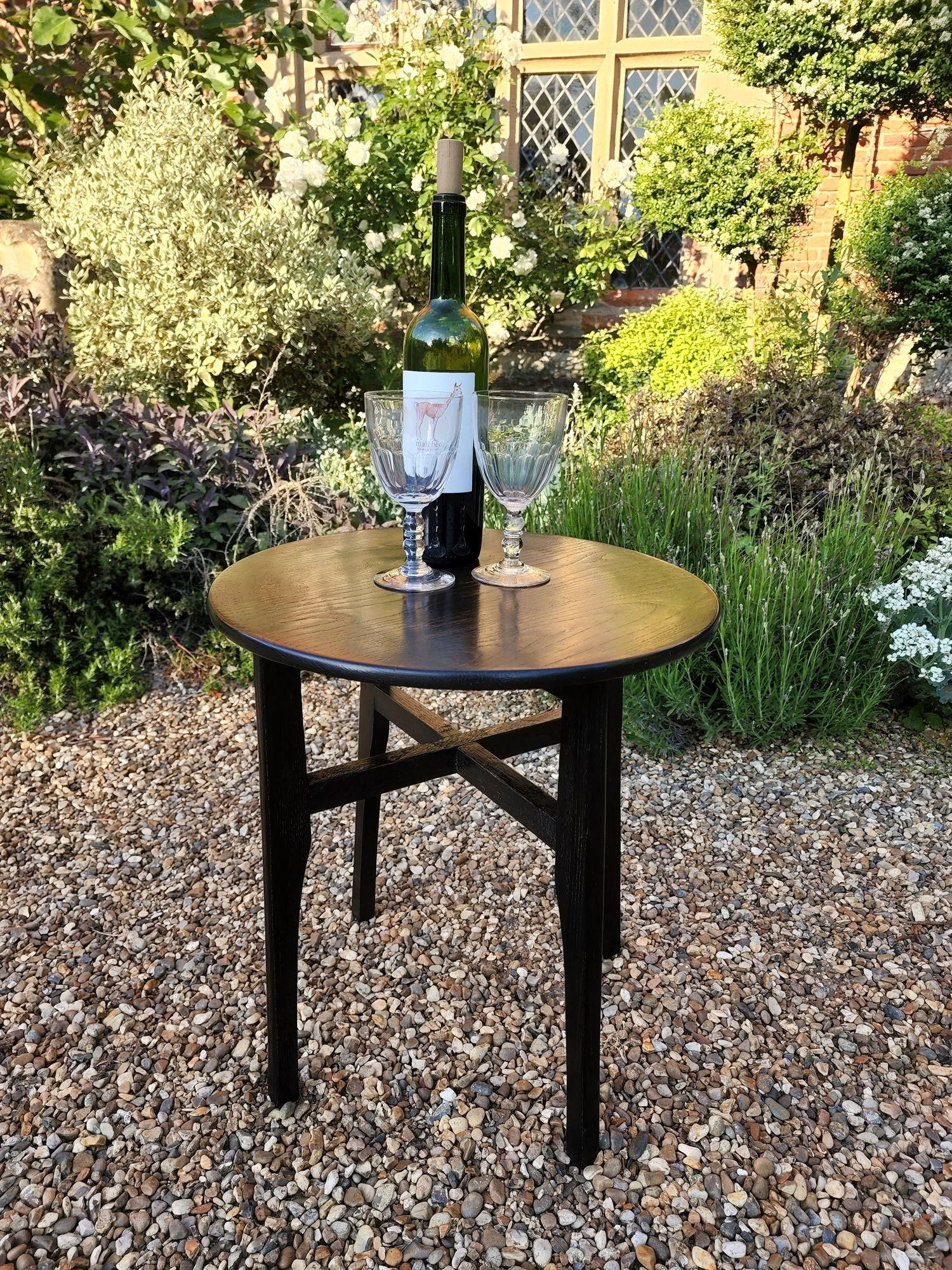A small wine table in darkened oak with circular top above cut-away legs joined by cross stretchers. Stylish and useful. England, circa 1920.