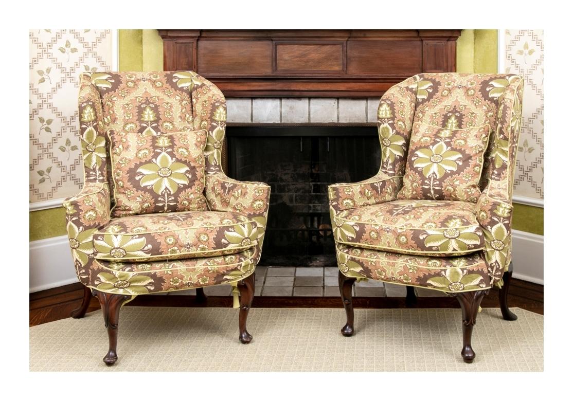 A fine pair of well made Wing Chairs with fine form and very comfortable. Clarence House fabric custom slip covers in an olive green and brown floral print. Vintage carved wing chairs with wide curved arms, raised on dark cabriole legs. The front