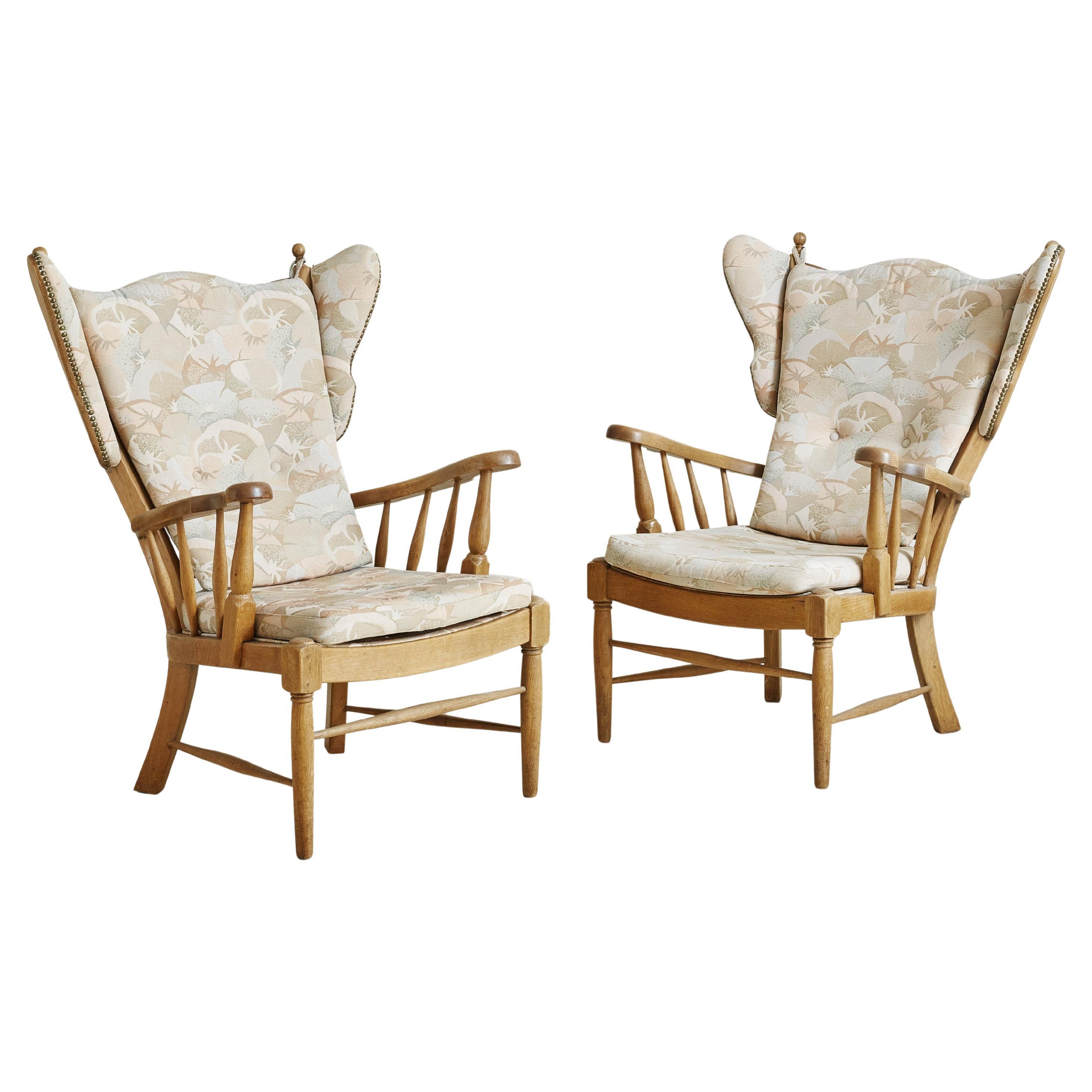 A pair of 1960s Danish Modern armchairs attributed to Regan Møbelfabrik Aarhus. These lounge chairs feature carved solid oak frames with high wingbacks, exaggerated ‘ears’, and angled windsor-inspired arms. We elected to keep the original botanic