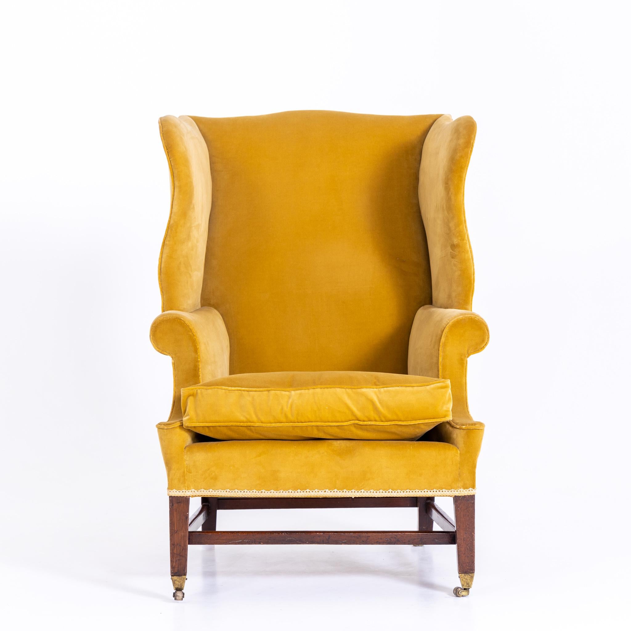 Yellow upholstered wingback armchair with high back on wooden frame with measuring castors.
