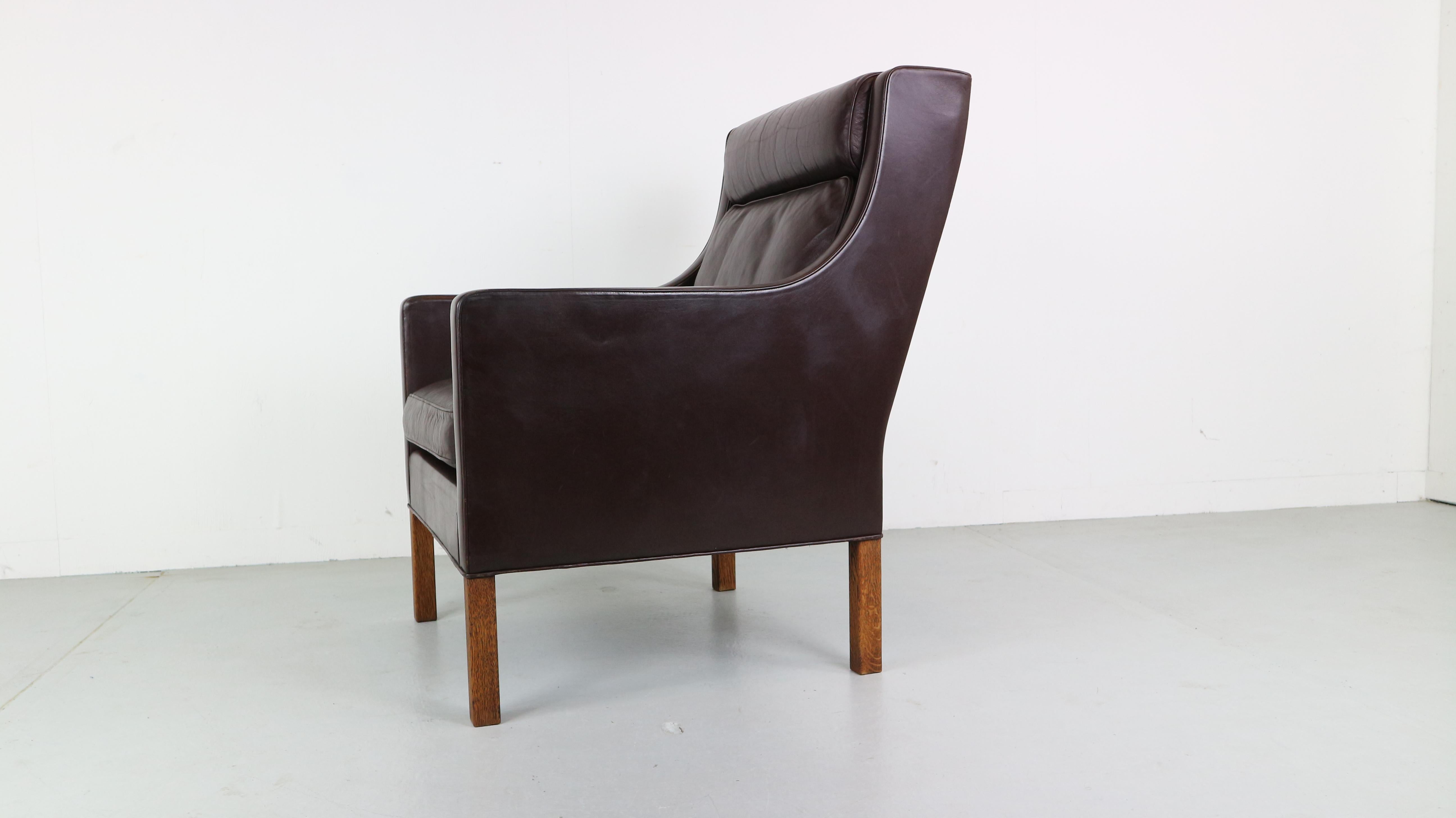 This model 2431 high lounge chair with deep-brown leather and solid oak legs was designed by Børge Mogensen in the 1960s. This lounge chair was made in the 1970s by Fredericia Furniture in Denmark and is very comfortable, with the cushions remaining