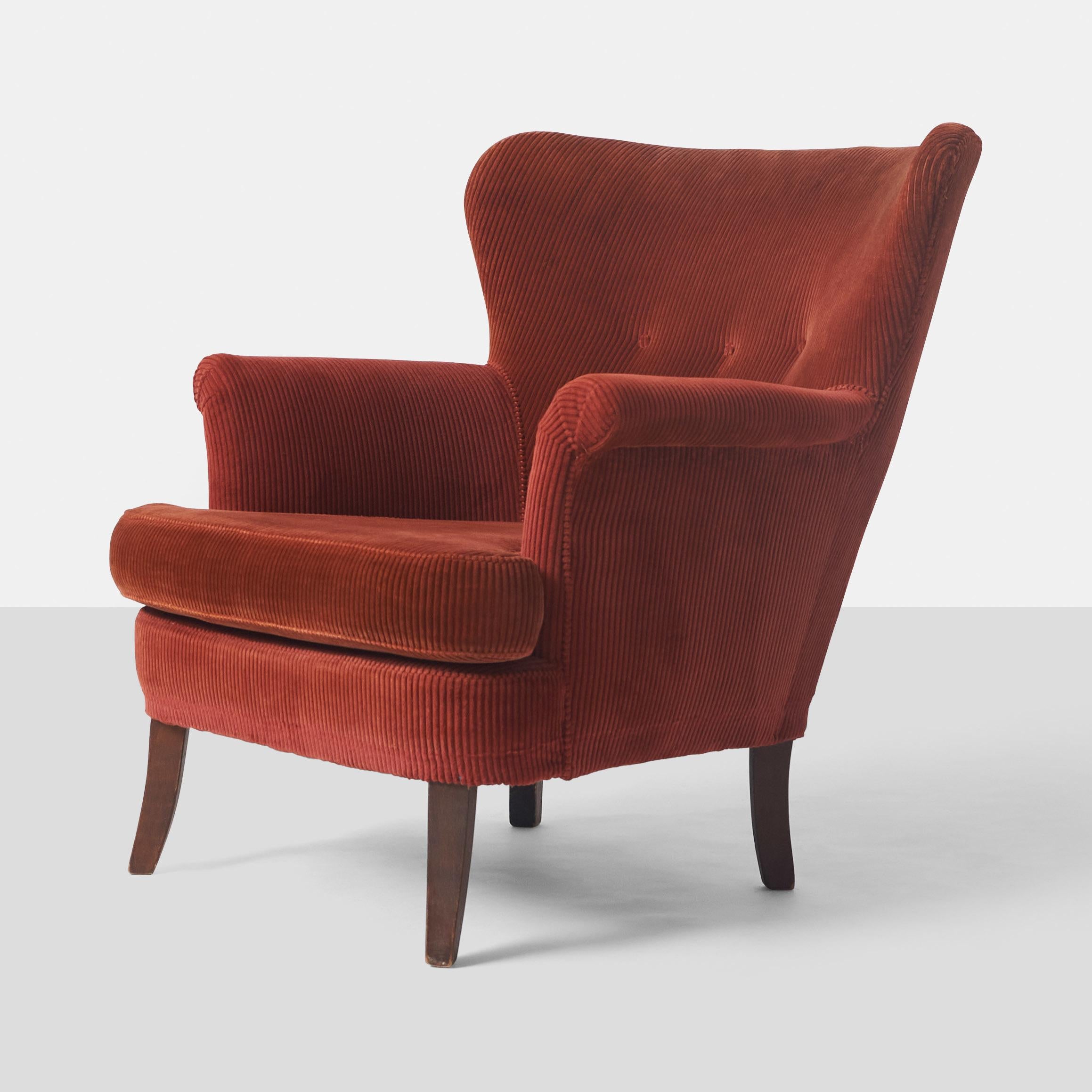 This low wingback lounge chair by Theo Ruth features a tufted back with three buttons, covered in a deep red corduroy fabric. Its teak legs are in good condition, with only minor scuffing, making it an ideal piece to reupholster.