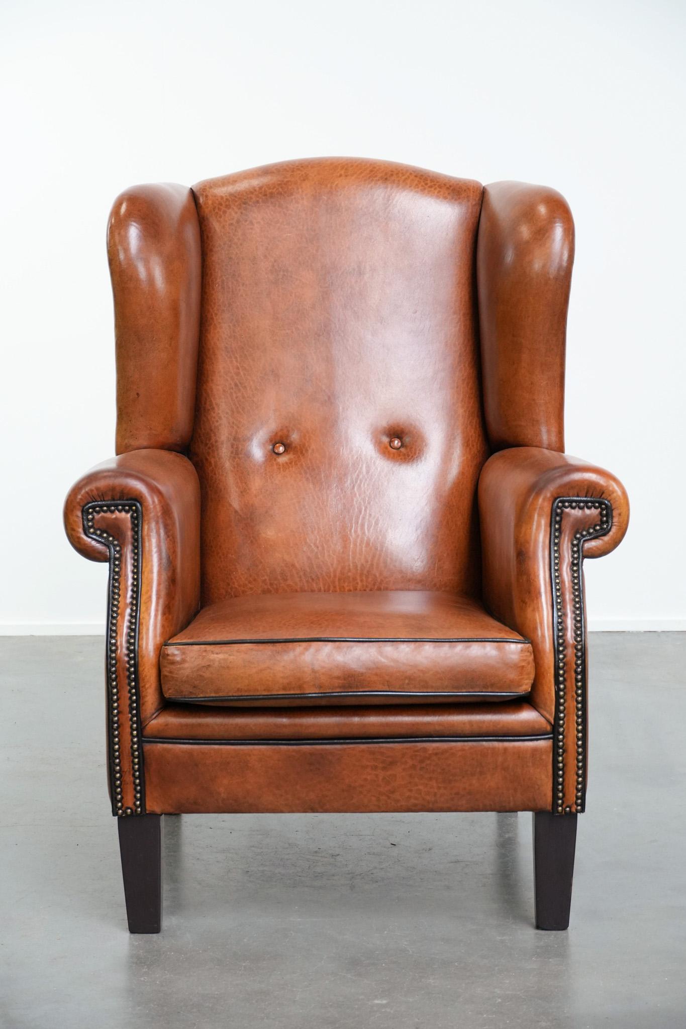 Ce superbe fauteuil à oreilles en cuir de mouton, dans une magnifique grande taille, est un ajout élégant et confortable à tout intérieur. La finition raffinée avec des passepoils noirs et des clous décoratifs confère au fauteuil un aspect