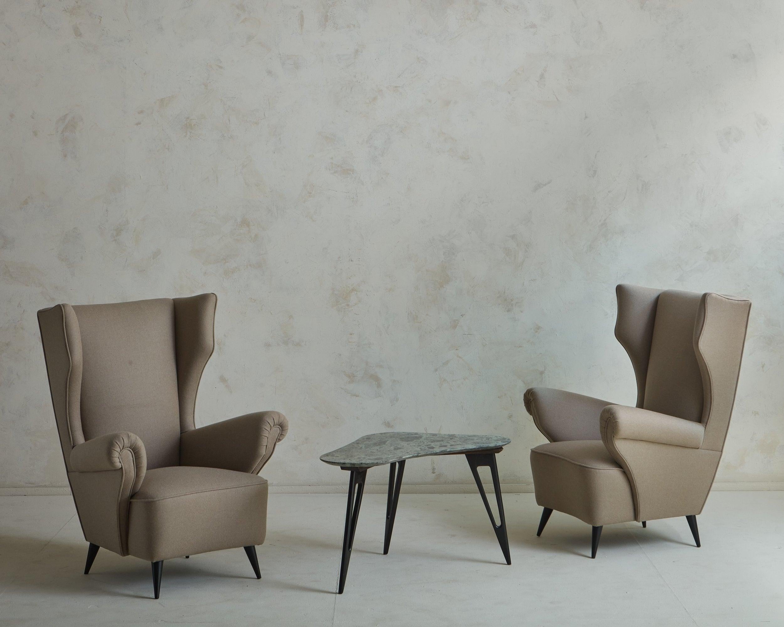 A 1960s Italian wingback lounge chair in the style of Paolo Buffa. This chair features a tall, dramatic backs and stately arms. It was freshly reupholstered in a taupe wool blend fabric with single welt detailing. The tapered wooden legs were
