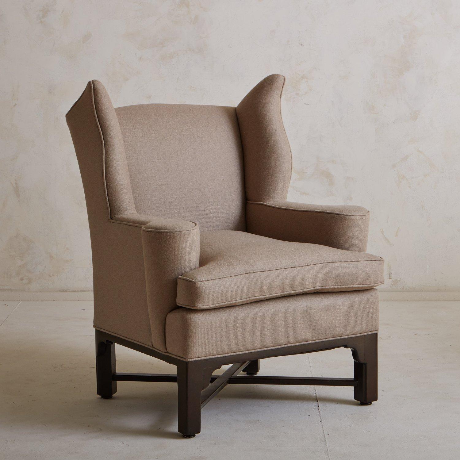 An antique German wingback lounge chair freshly upholstered in a taupe wool-blend fabric with a subtle striped detail and single welt detailing. This chair has a wood X-base stained a beautiful dark brown hue. We love the dramatic curved wings and