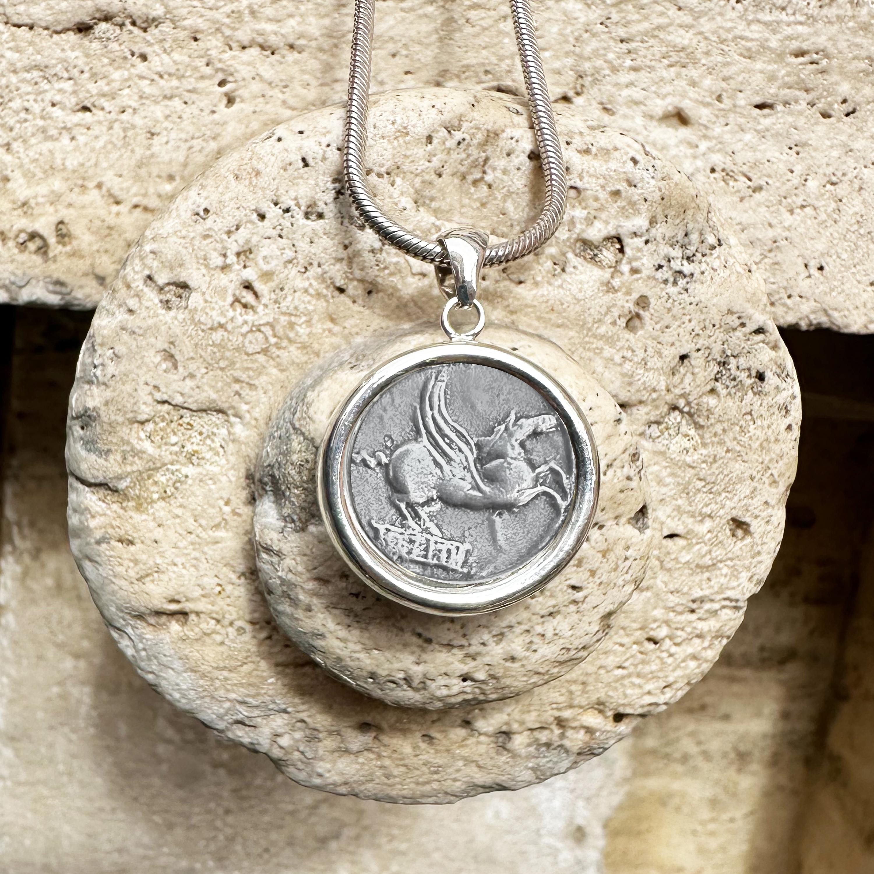 This sterling silver pendant holds an authentic Greek coin dating back to 90 BC, featuring a depiction of Pegasus, the legendary winged horse. On the reverse side of the coin, you can see Mutinus Titius, an ancient Roman deity associated with
