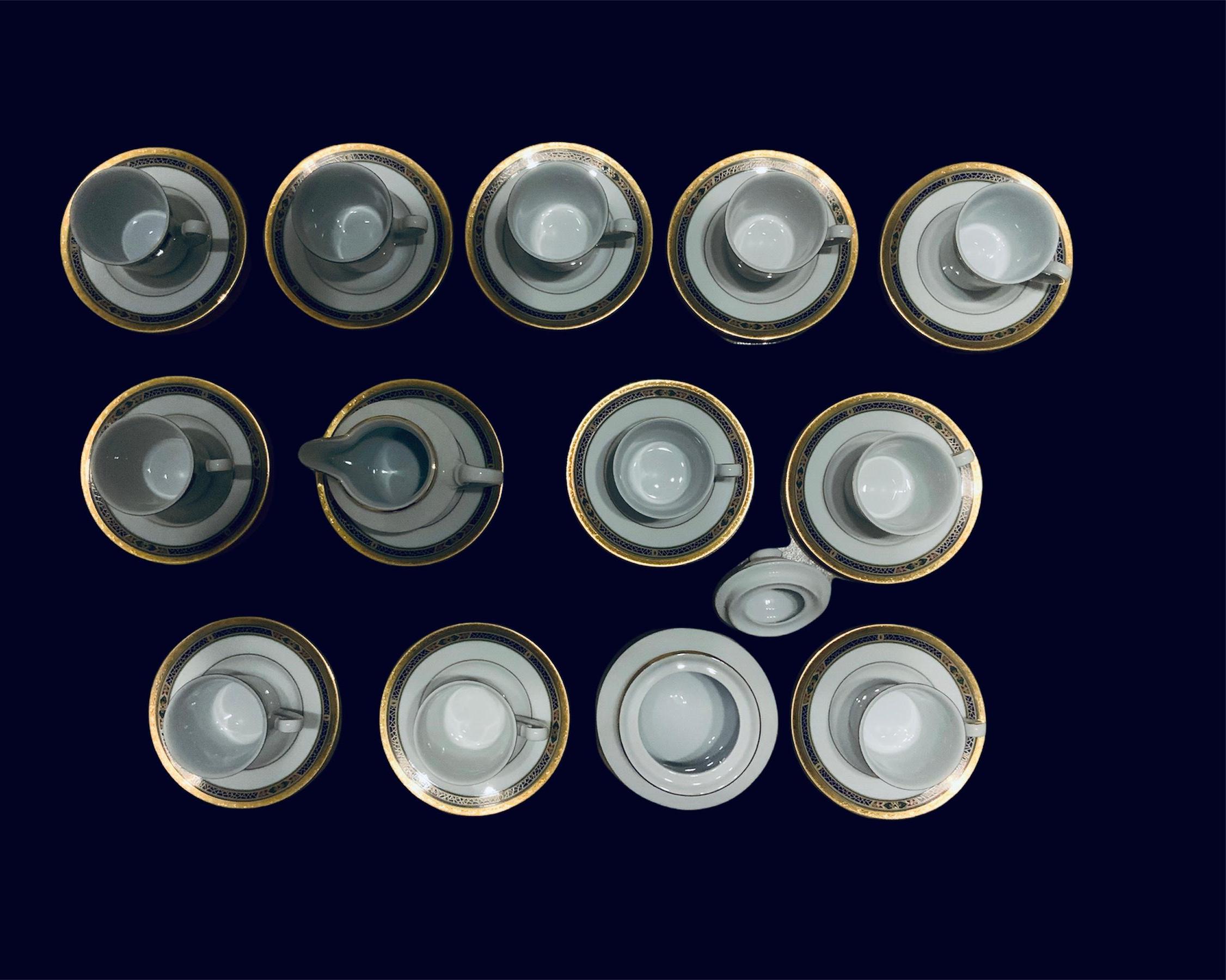 This a Winterling Marktleuthen Bavaria Porcelain Set of eleven demitasses, twelve saucers, a creamer and a sugar bowl. They have a white color background with gold borders that are decorated with scrolls. Below it, there is a band with blue mosaics