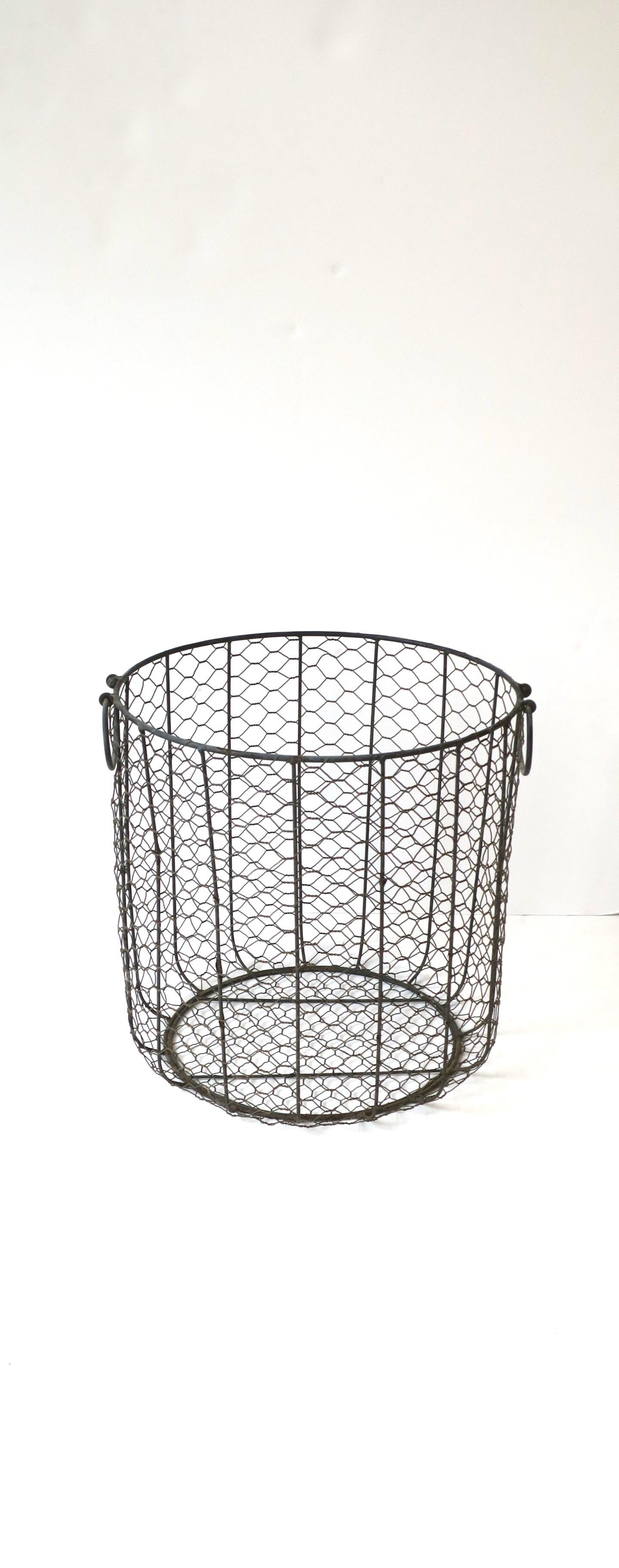 A metal wire basket, circa early-20th century. A great piece for a fireplace to hold firewood or for a bathroom or pool area, etc., to hold towels. Demonstrated holding bath towels. Piece is round with handles. Dimensions: 13.88