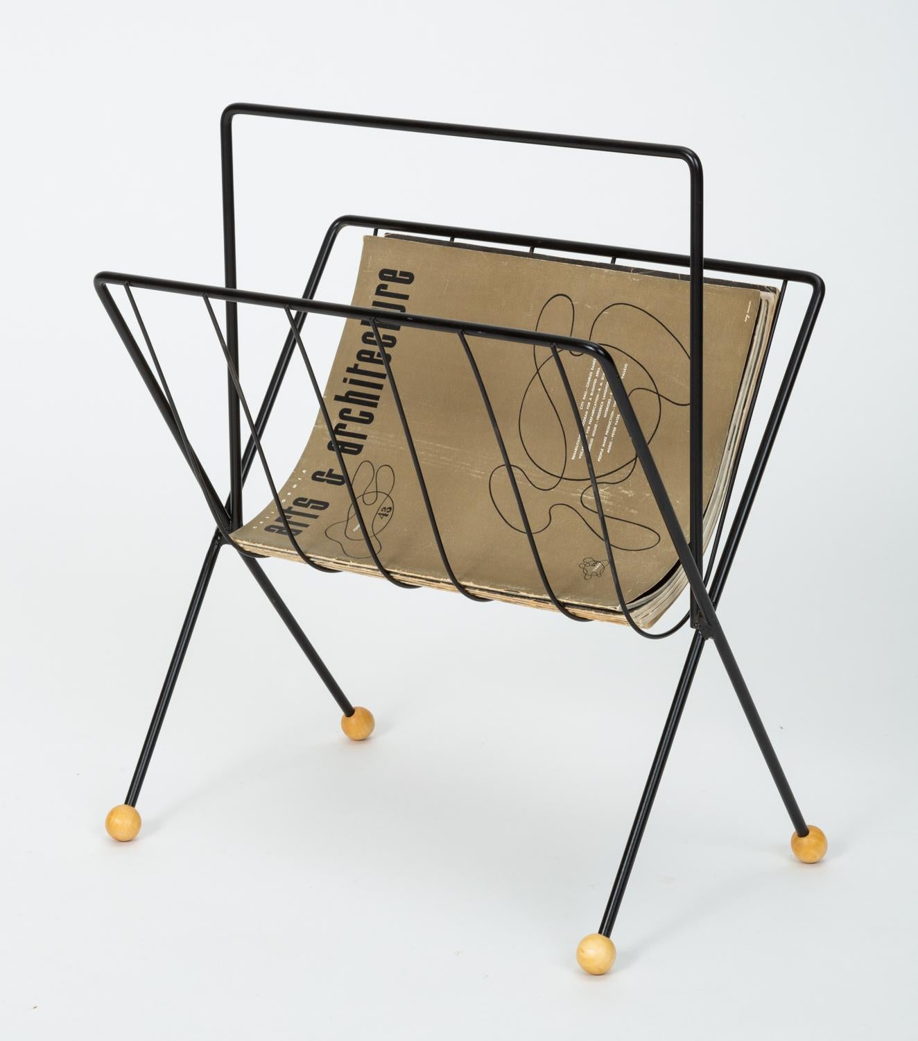 American made wire magazine rack by New York-based designer Tony Paul. The rack has a skeletal frame with bent spokes to hold your items and crossed legs finished with wooden ball glides. The piece has been powder-coated for a glossy black