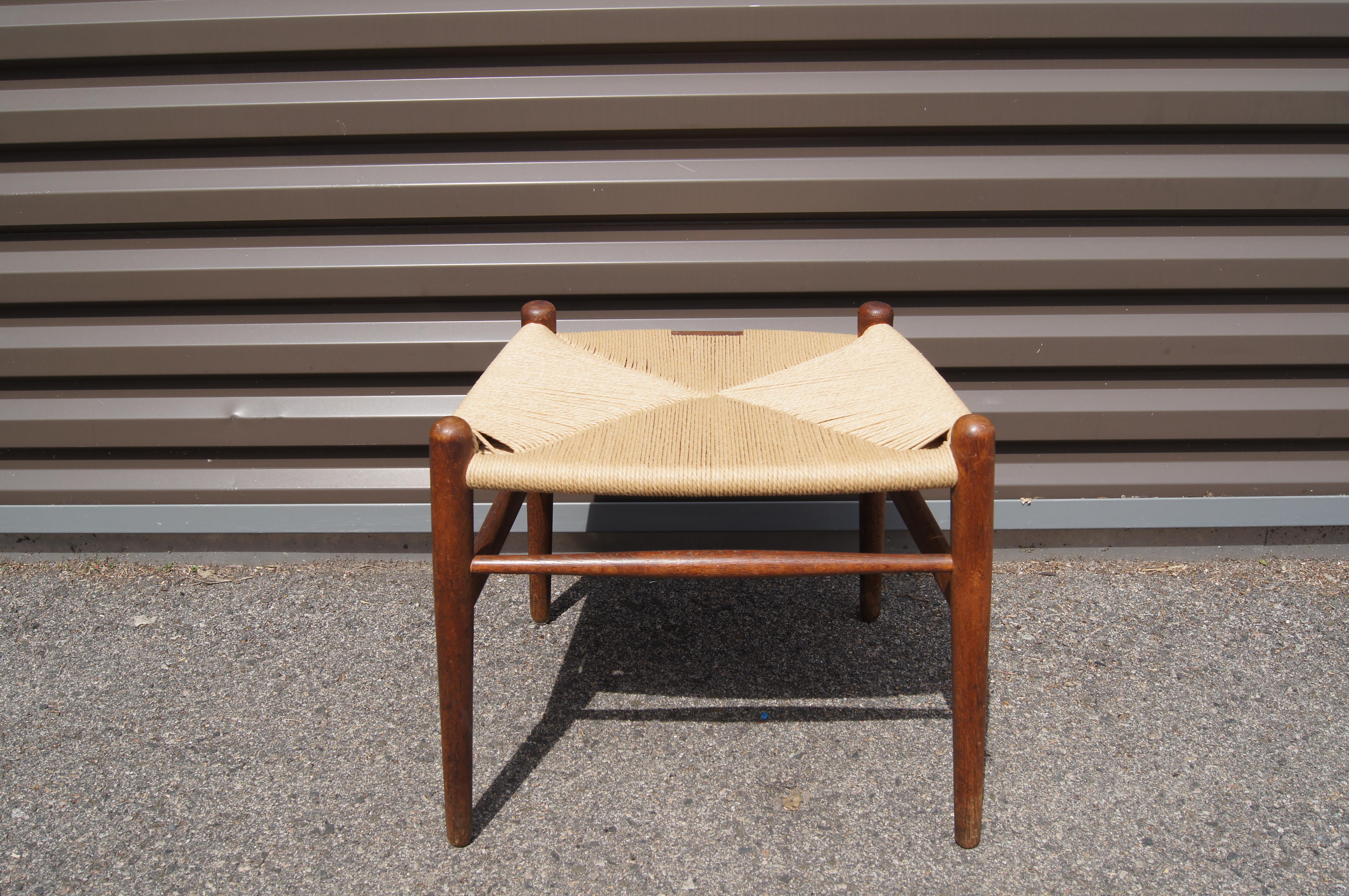 Hans Wegner designed this rarely seen ottoman to accompany his Wishbone seating for Carl Hansen. The original tapered oak frame features a papercord seat, newly wrapped.

Manufacturer's label on underside.