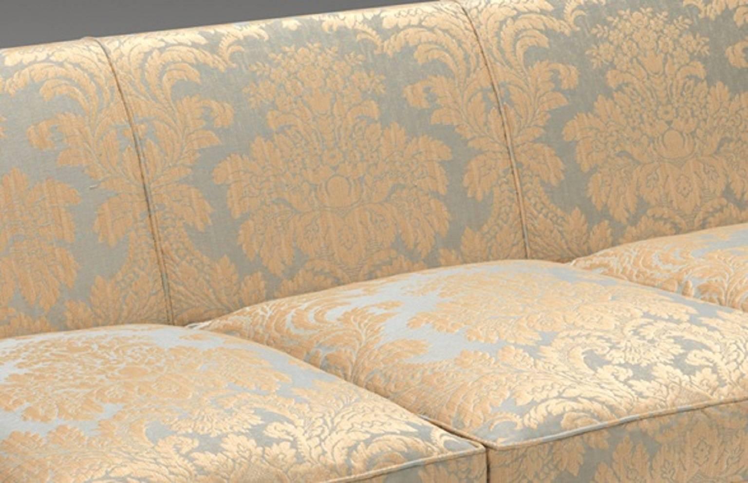 A George IV design sofa with square padded back and out scrolled arms and squat seat. The channelled arm supports and front seat rails with applied carved and gilded rosettes on spirally turned tapering legs terminating in brass castors. 

Covered