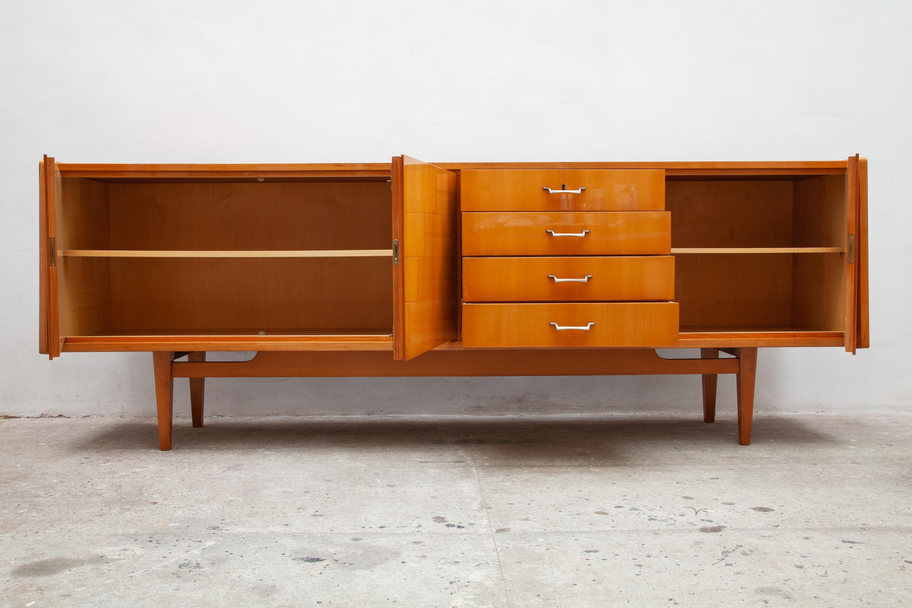 High gloss credenza made of citrus wood. 
This piece is German manufacture for the Italian market. 
Features two cabinet compartments with shelves and a set of 4 drawers. 

The top drawer is felted for silverware and has the original key.
In