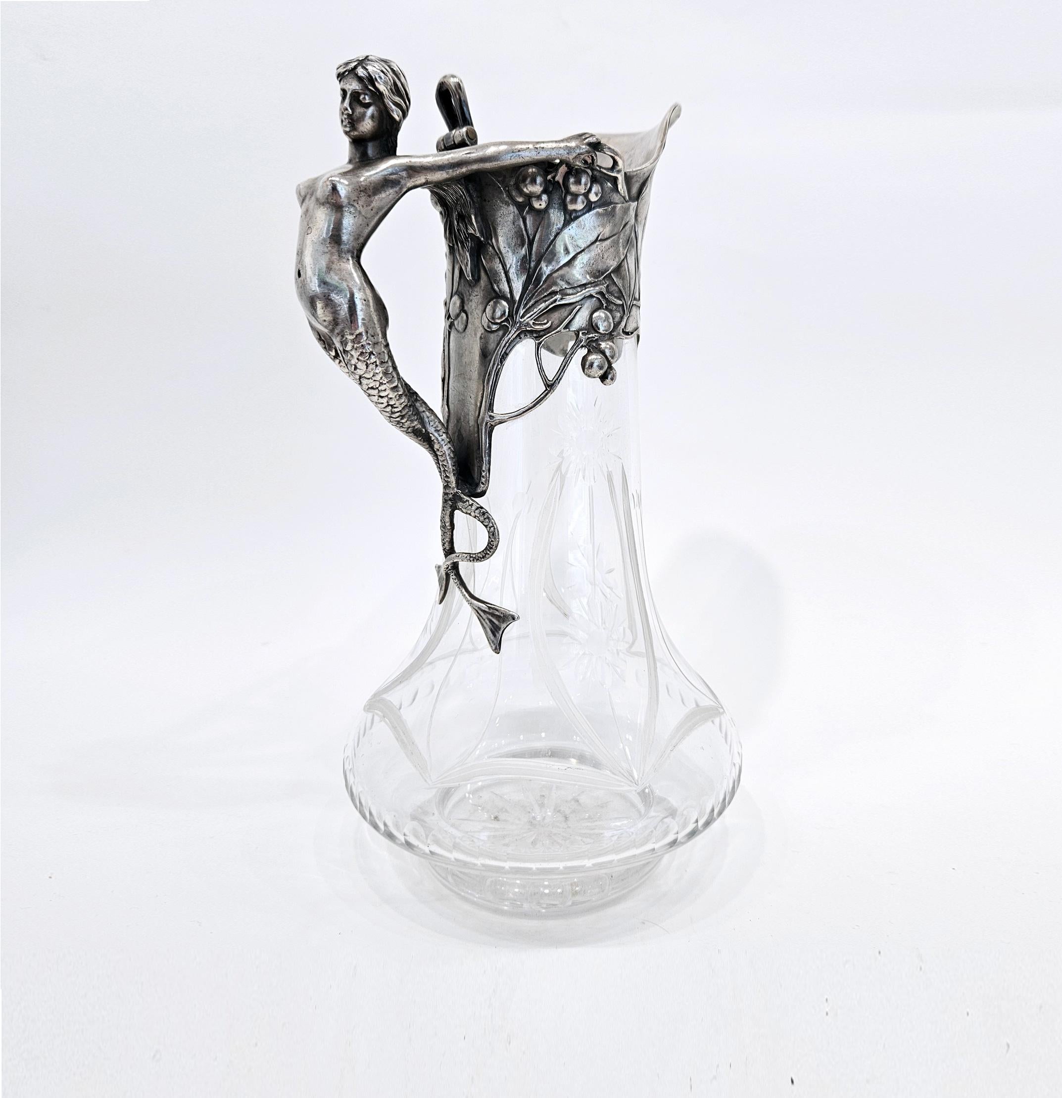 Une carafe art nouveau de belle qualité fabriquée par WMF (Wurttembergische Metallwarenfabrik) en Allemagne vers 1901. 

La monture en métal argenté est ornée d'une sirène en guise d'anse, qui s'accroche à la monture du col de la carafe, ornée d'un