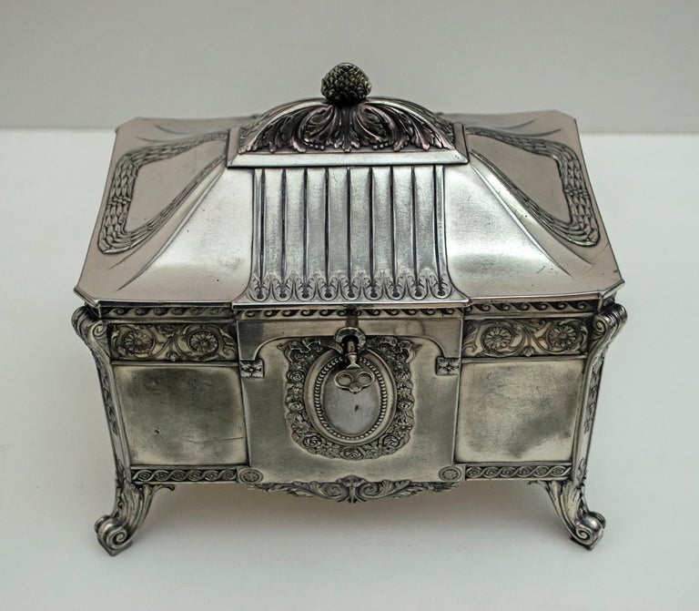 Jewelery box, WMF - Germany, early 20th century
Rectangular shape with scroll decorations, surmounted by a crown, internal fabric compartments, four curled feet, brand under the base. Interior lined in fabric, faded and has tears. Complete with key