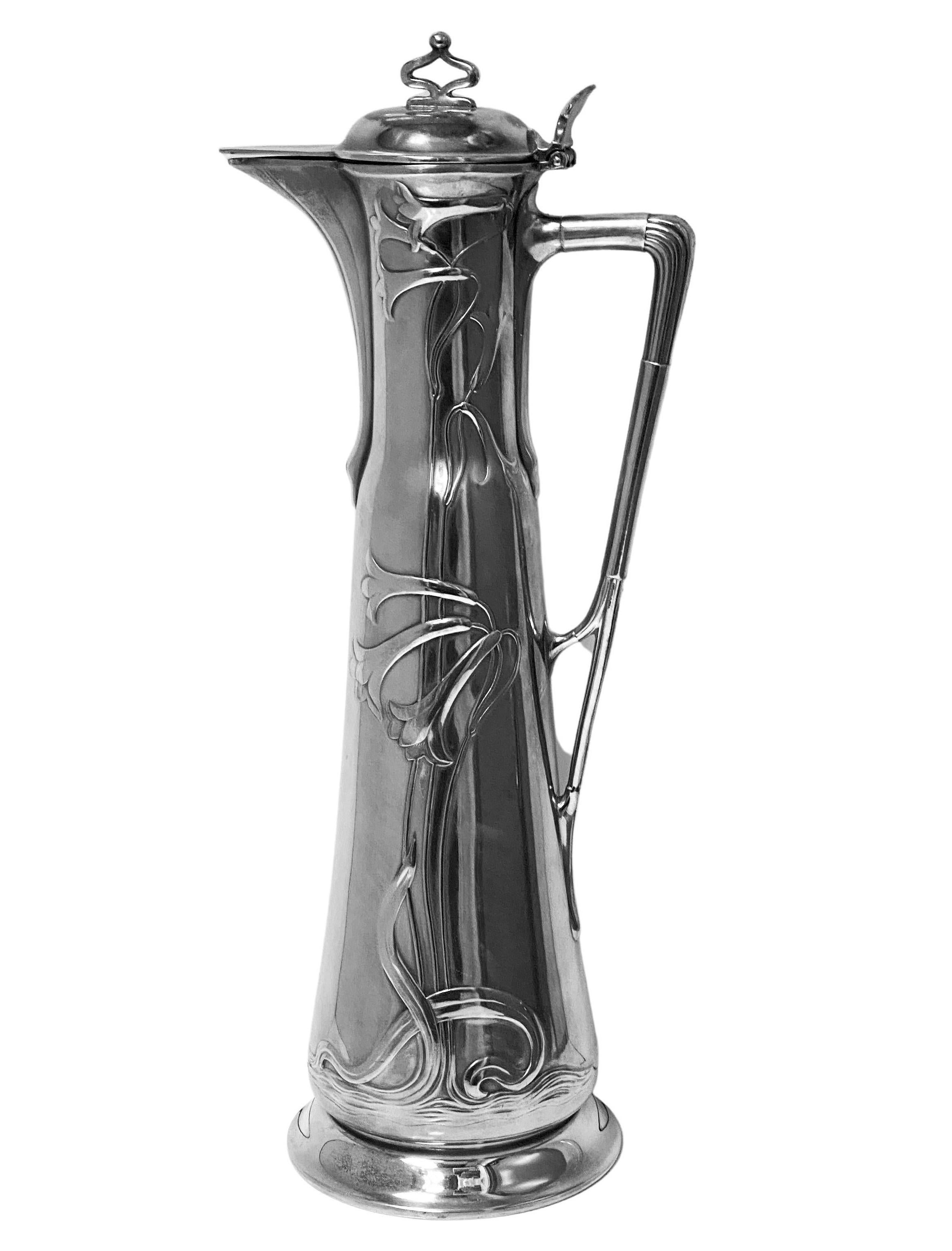 WMF Art Nouveau Jugendstil Pewter Claret Wine Jug C.1900. Large tapering body decorated with stylised foliate relief, with hinged lid and stylised handle stamped WMF O/1 to base. Height: 14.50 inches. Width: 6 inches. Condition: very slight wear to