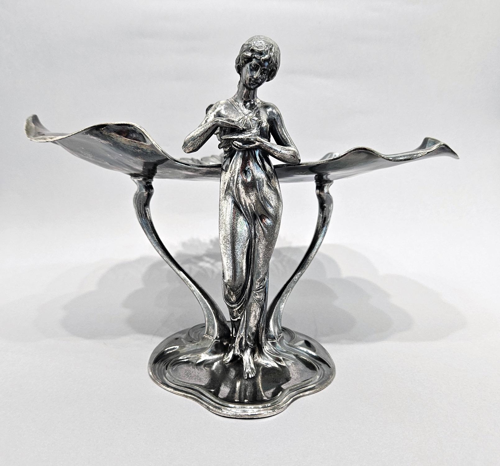 Un bellissimo vassoio o tazza da centrotavola in argento Jugendstil in stile art nouveau con una ninfa che tiene in mano una colomba, realizzato da WMF in Germania nel 1910 circa.  

Si tratta di uno dei pezzi più iconici della metallurgia WMF,