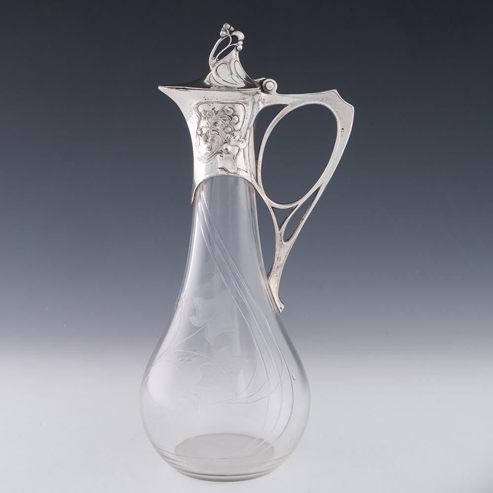 Überschrift:  WMF Claret Krug mit versilberter Halterung
Datum : um 1905
Zeitraum : Wilhelm II.
Herkunft : Geislingen, Deutschland
Verzierung : Fruchtige Rankenverzierung auf Silber und Glas. Naturalistischer eckiger Griff. Bezeichnet mit WMF