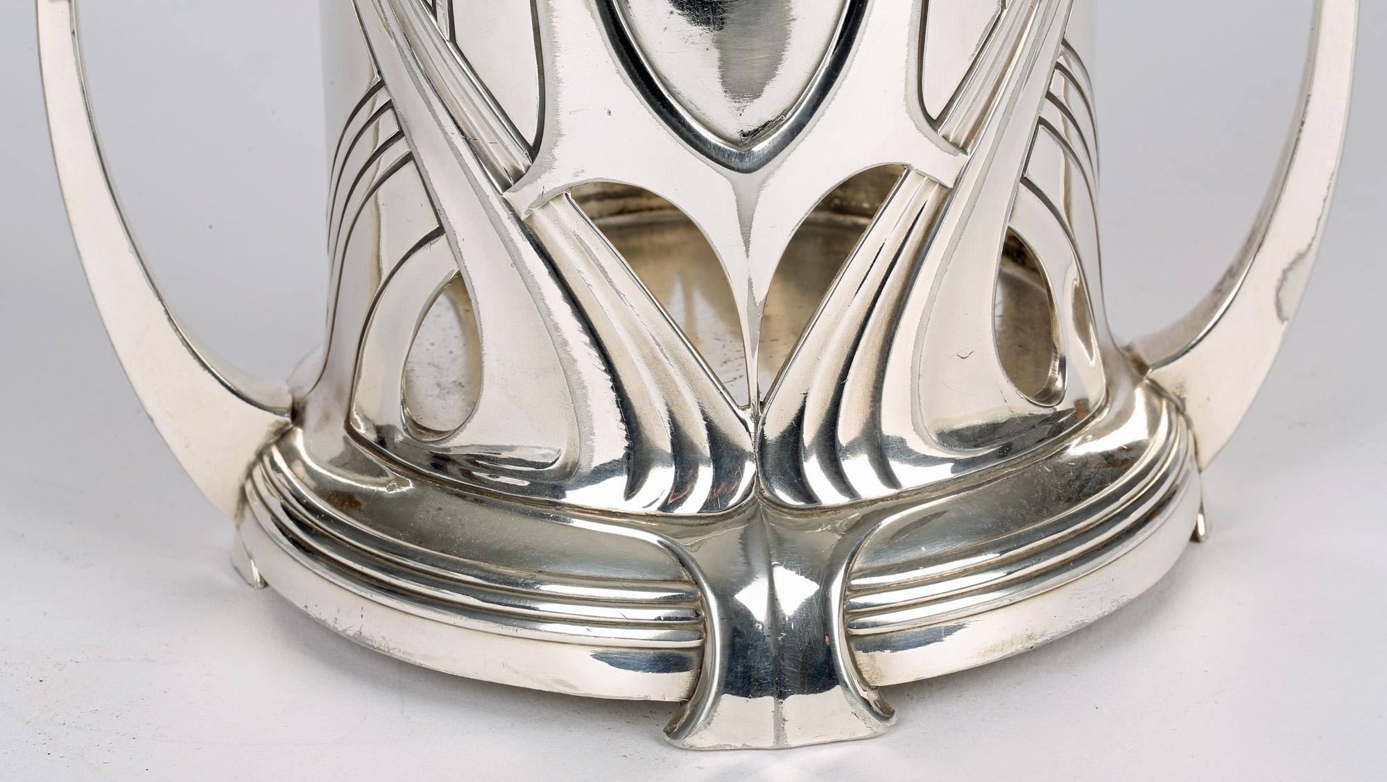 A stunning German jugendstil silver plated twin handled soda syphon or bottle holder made by WMF (Württembergische Metallwarenfabrik) and dating from circa 1906. The holder is of rounded cylindrical shape standing raised on four feet on a wide