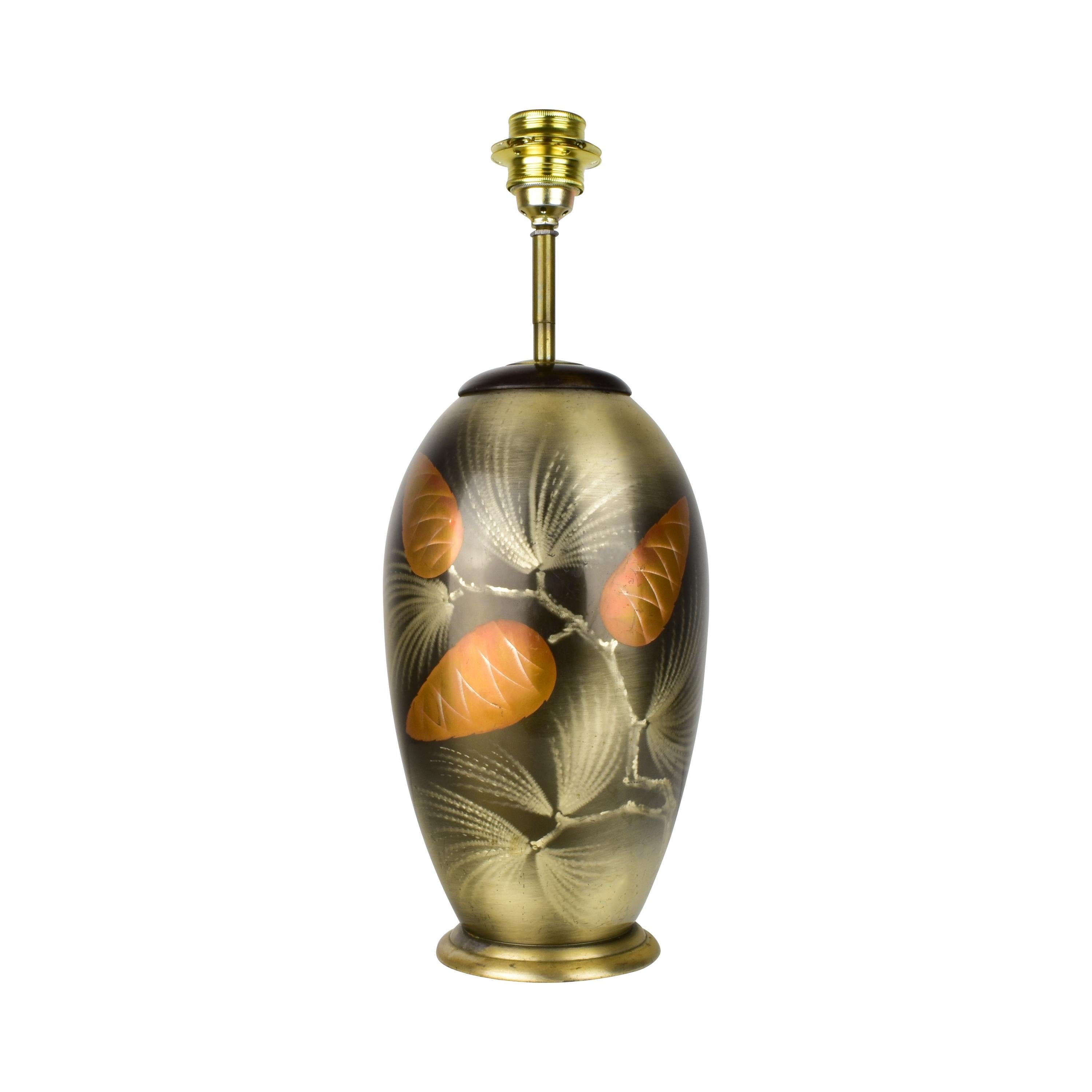 A very rare Art Deco WMF Ikora table lamp featuring a decorative pinecone design. The body is made of silver-plated brass and showcases a stenciled airbrush motif. The lamp has a classic, elegant look with golden and warm tones highlighting the