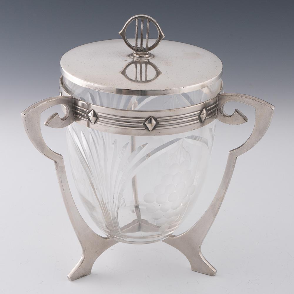 Heading : WMF silver plate Art Nouveau biscuit box c1910
Period : Wilhelm II
Origin : Geislingen, Germany
Decoration : Successionist type frame with curved angular stand and geometric banding to collar. Glass with cut arches and fans with fruiting