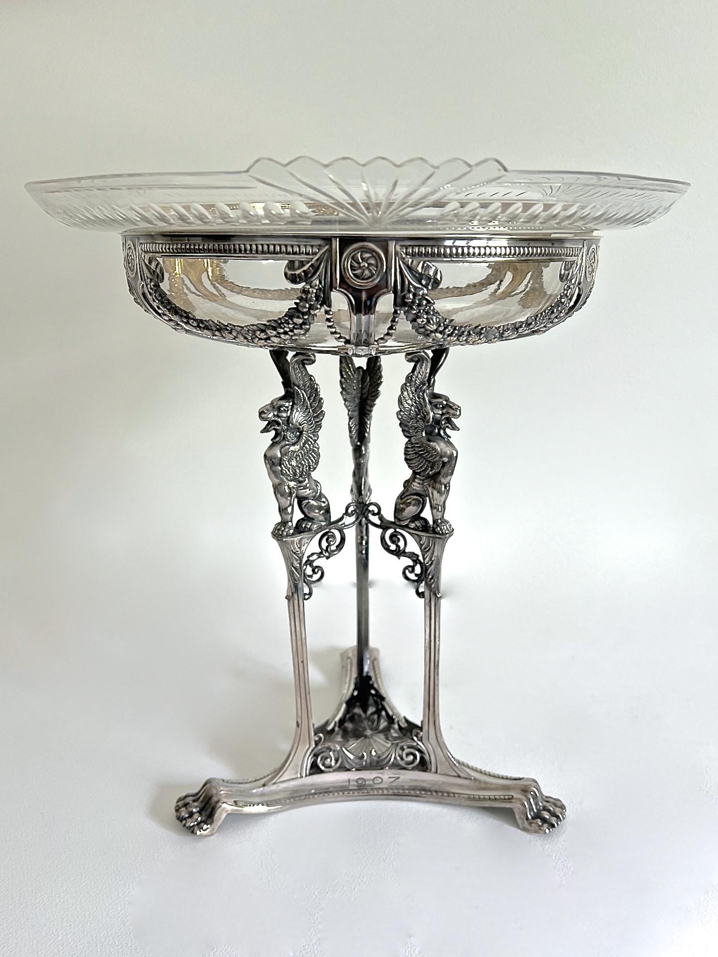 A stunning WMF silvered metal & cut glass centerpiece in the Neo Classical style. The tripod stand cast with Classical motifs such as floral swags, Gryphons, paterae, scrollwork, beading and lion paw feet. The interior is gilt washed. The stand