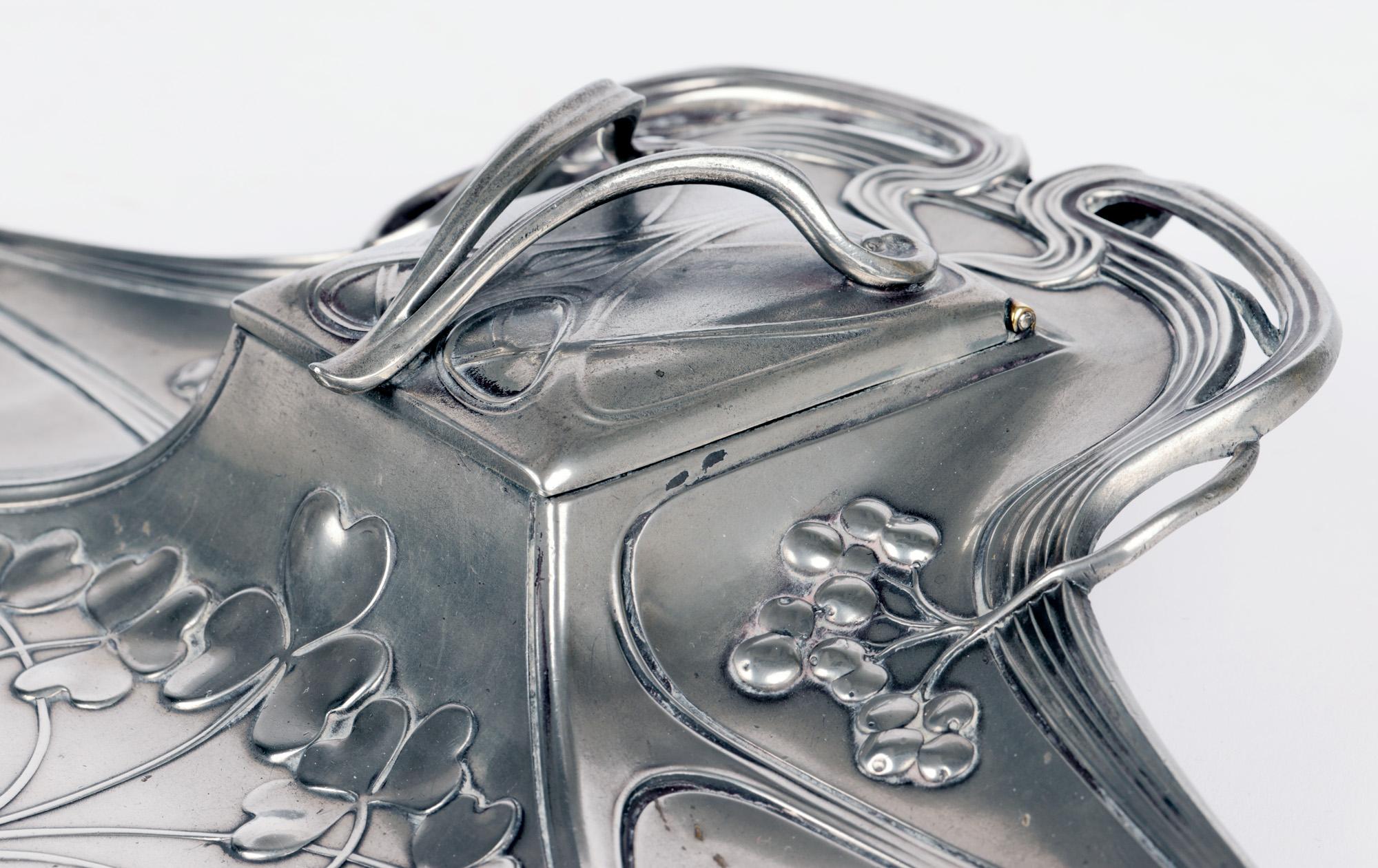 A very stylish German Jugendstil pewter desk stand and inkwell by renowned makers WMF (Württembergische Metallwarenfabrik) and dating from around 1906. The stand comprises of a central raised inkwell with square top and hinged cover applied with a