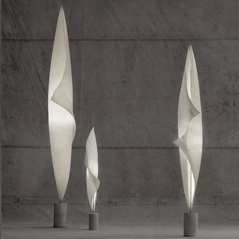 Wo-Tum-Bu 1 floor lamp is part of the Mamo Nouchies collection by Ingo Maurer. The collection utilizes classic Japanese pleated paper techniques combined with a raw yet refined concrete base and metal stem to support the shade.