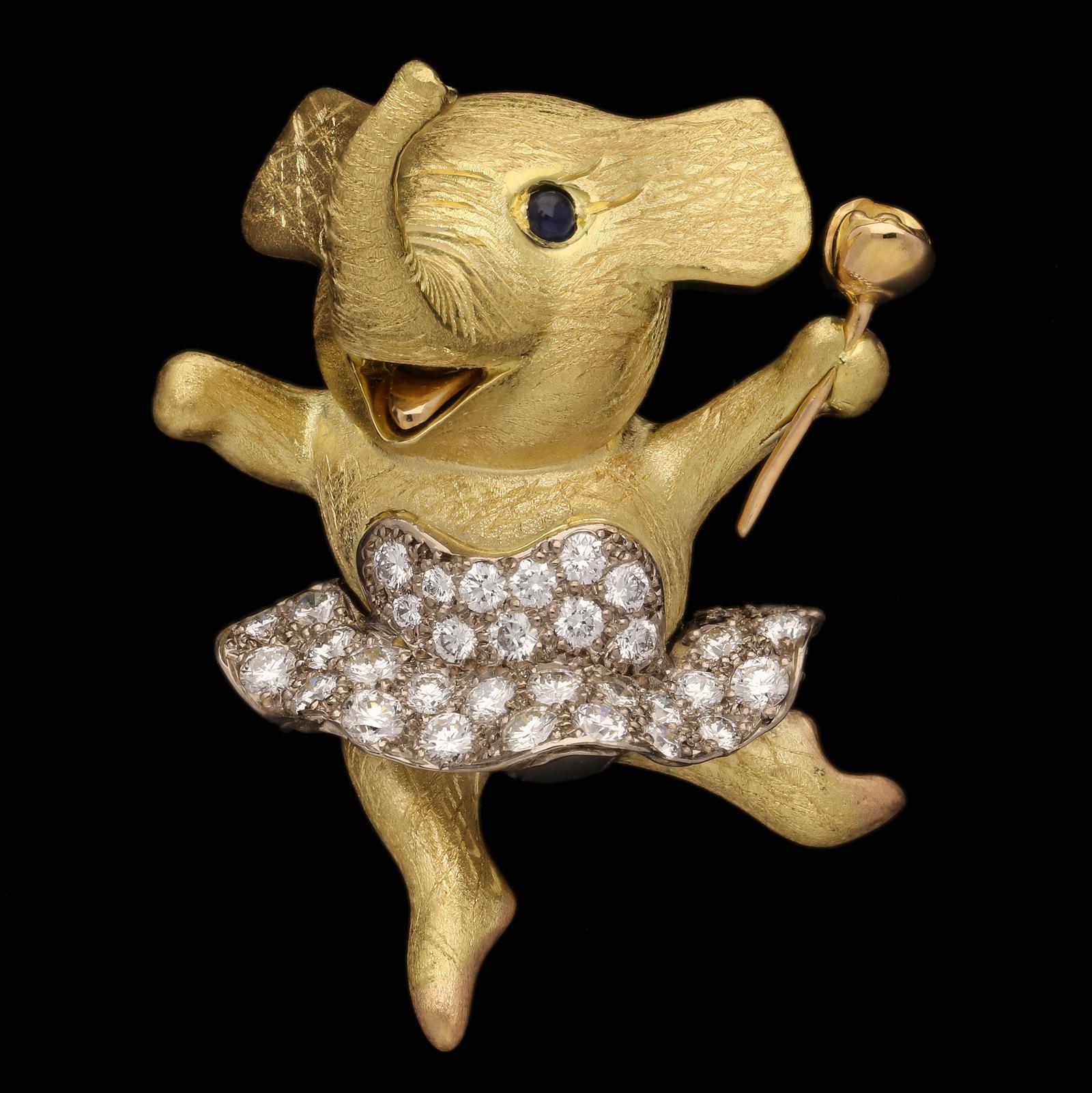 Description
A delightful elephant ballerina brooch by E.Wolfe & Co. 2021, the finely modelled elephant in 18ct yellow gold with semi-matte finely textured finish wearing a diamond set tutu and depicted leaping through the air with arms thrown wide,