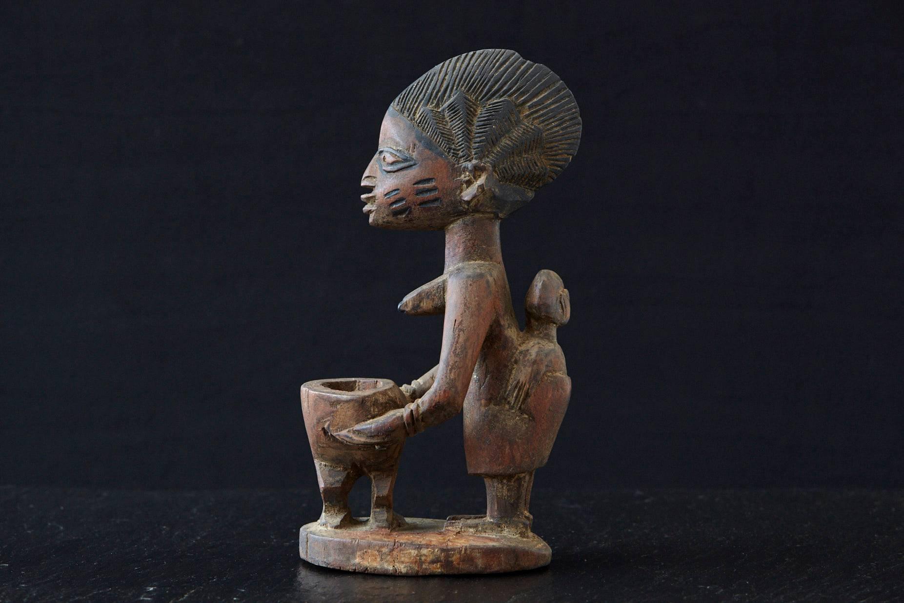 Carved wooden sculpture depicting a woman sacrificing holding an offering bowl, Yoruba People,
Nigeria, 1940s

There is a small old chip on the top, please refer to the photos. 

The numbers are the inventory numbers from Pennsylvania State
