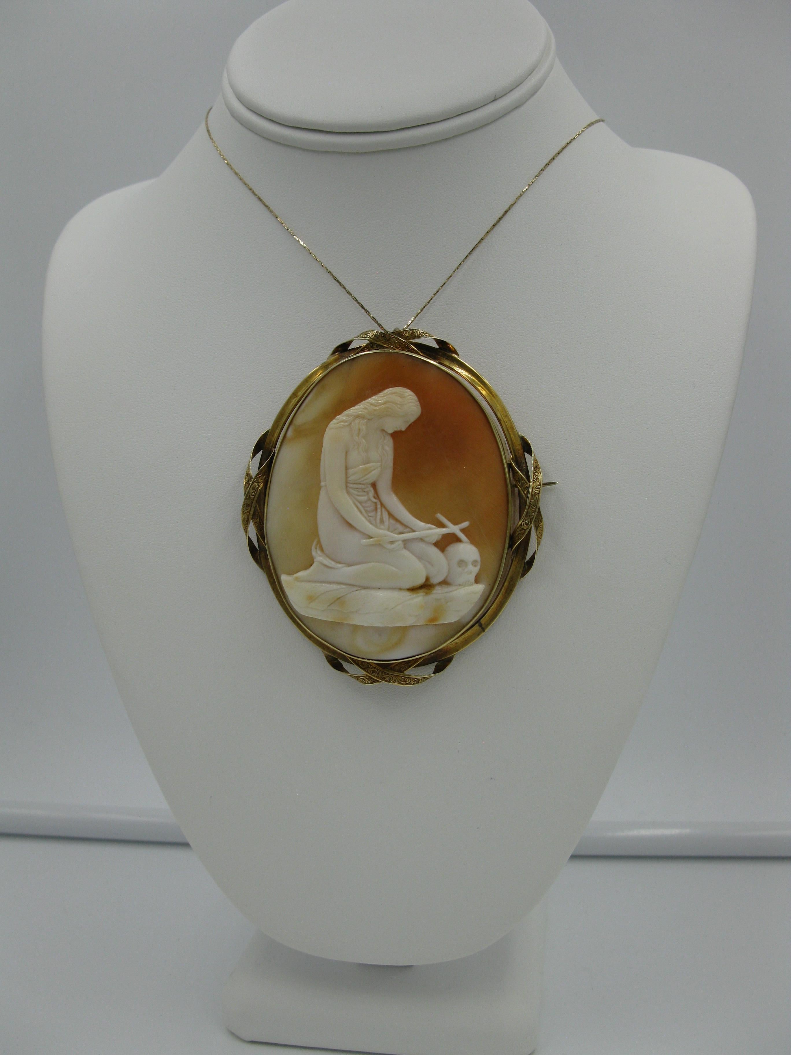 AN ABSOLUTELY STUNNING AND VERY RARE MUSEUM QUALITY VICTORIAN SHELL CAMEO PENDANT OR BROOCH DEPICTING A KNEELING WOMAN WITH A CROSS AND A SKULL - THE MONUMENTAL CAMEO IS 3 1/4 INCHES TALL.  THE CAMEO IS SET IN A MAGNIFICENT SCROLLWORK ENGRAVED 14