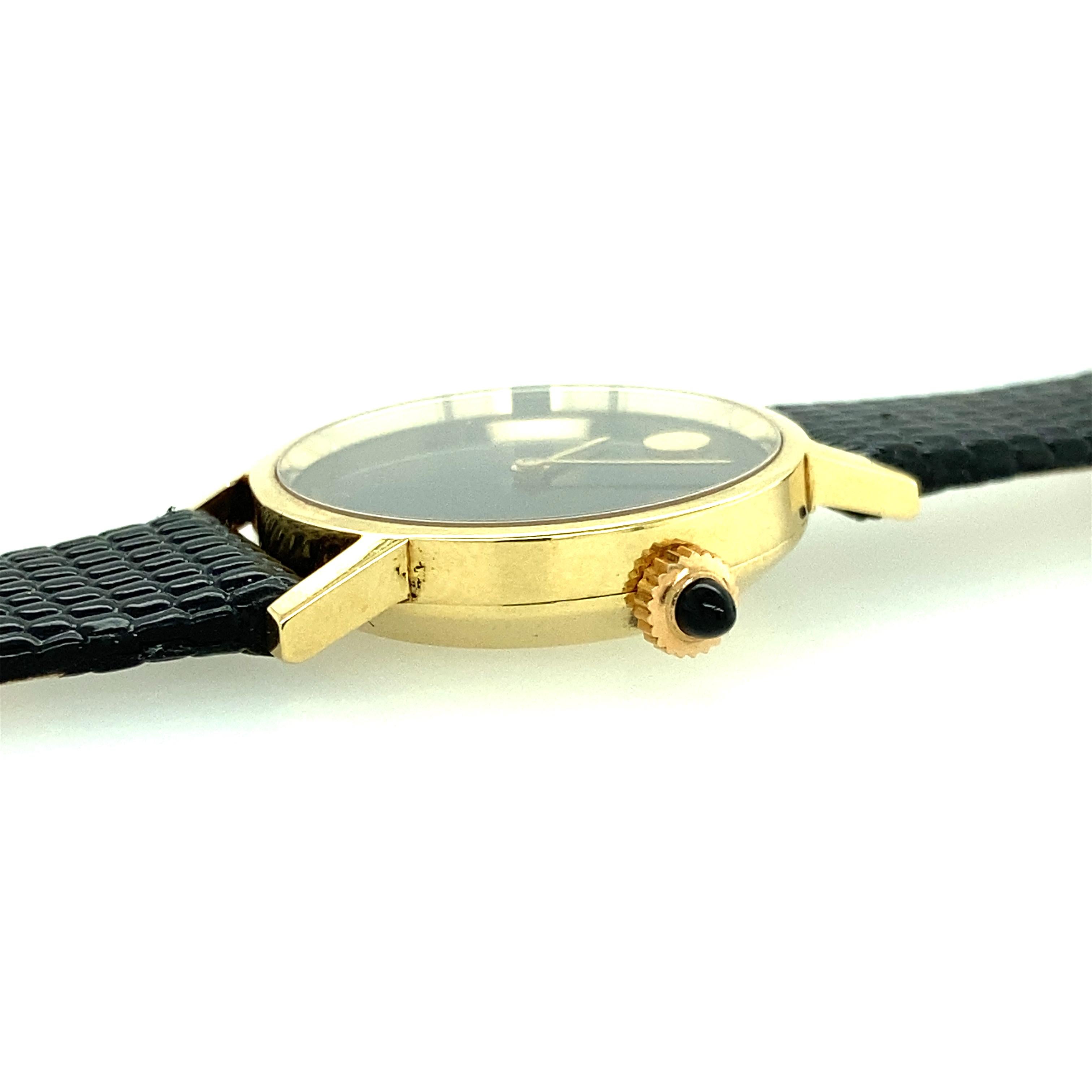 Eine Movado-Uhr aus 14 Karat Gelbgold mit Zenith-Uhrwerk. Die Uhr misst 24::30 mm im Durchmesser und ist acht Zentimeter lang. Das Armband aus echtem Leder misst an der Vorderseite der Uhr 12 mm und verjüngt sich zum Ende des Armbands hin auf 9::61