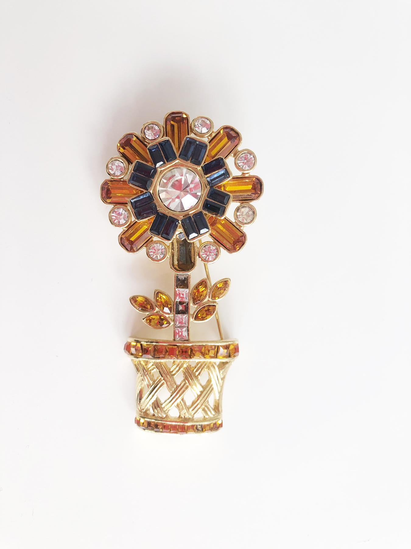 Elegant brooch by the famous stylist Valentino from Italy 90s. The brooch is shaped like a vase with a well-defined flower. The design of the vase is reproduced by metal weaving and the flower is set with various yellow and blue coloured stones. On