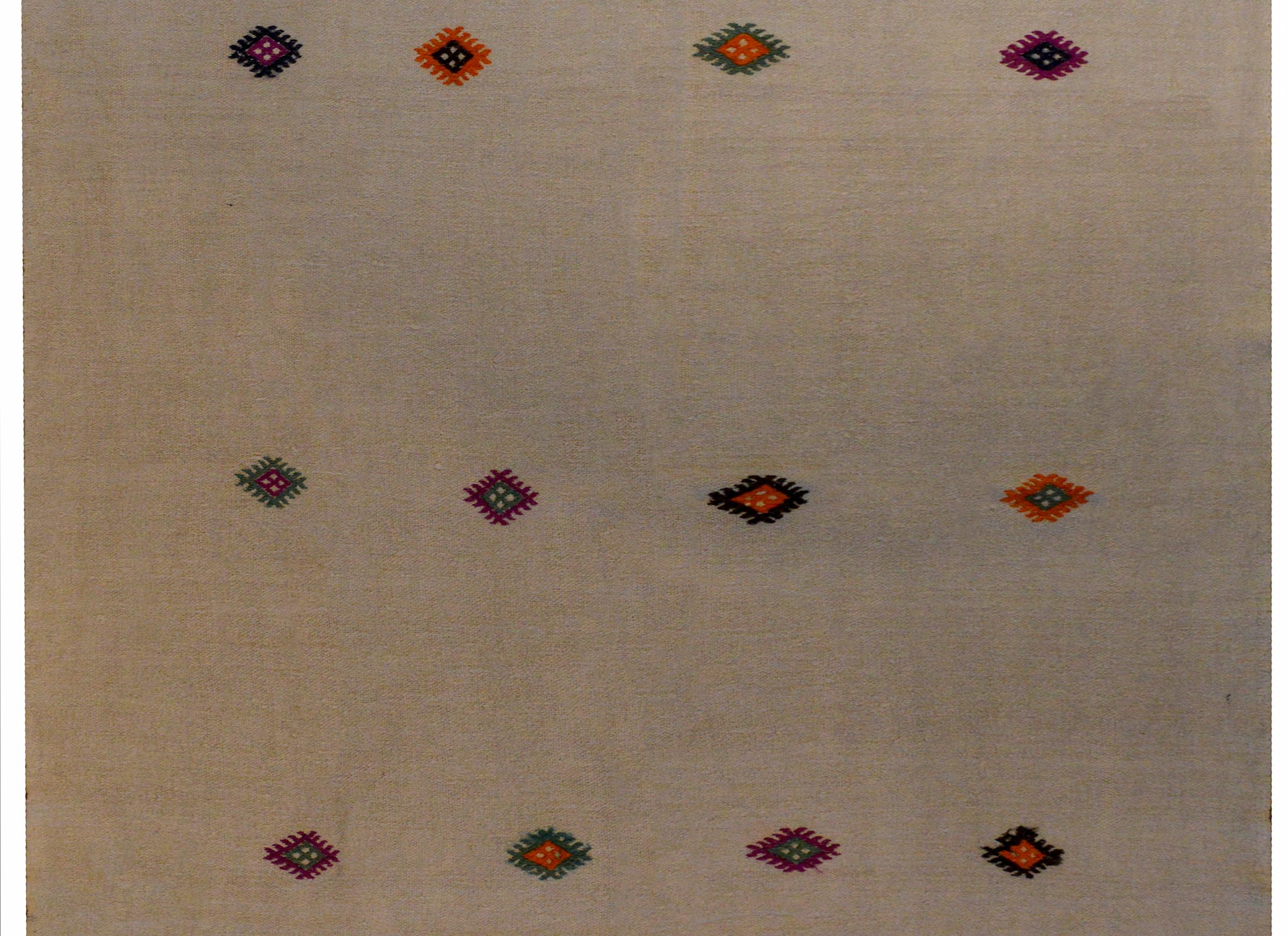 A wonderful mid-20th century Turkish Konya kilim rug with a simple pattern of stylized diamond medallions woven in crimson, green, violet, and gold vegetable dyed wool on a natural undyed cream wool background.