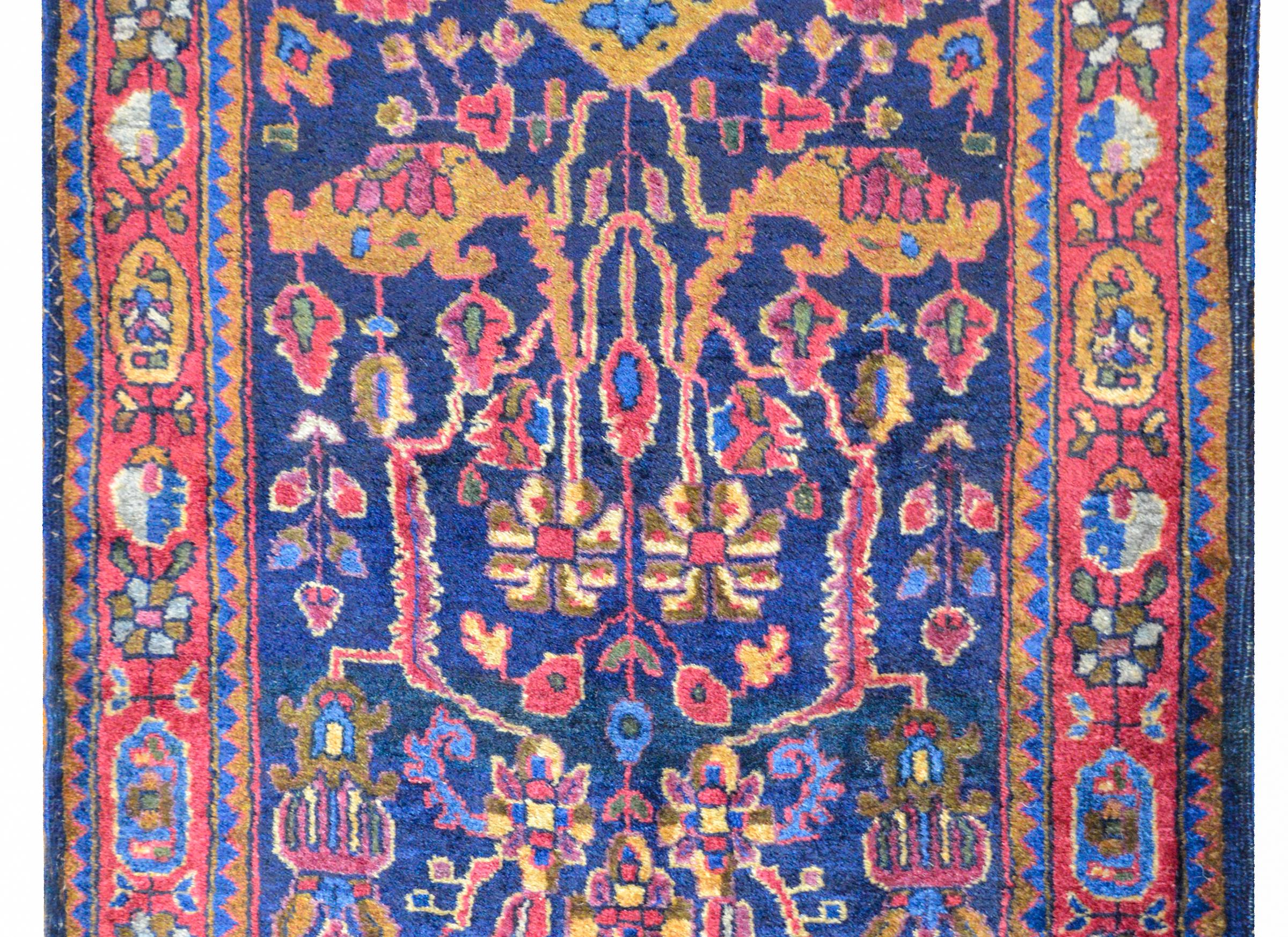 A wonderful early 20th century Persian Kashan rug with an all-over tribal floral and vine pattern woven in gold, light indigo, coral, brown, and cream, on a dark indigo background, surrounded by a complex floral patterned border flanked by pairs of
