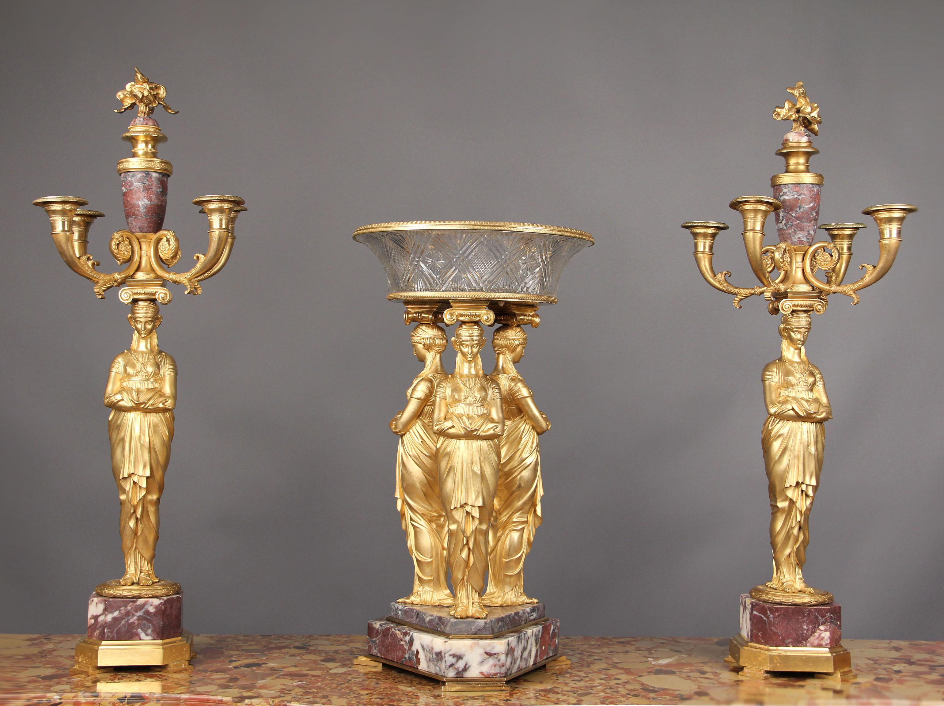A fantastic late 19th century Empire style gilt bronze and Fleur de Pecher marble three-piece garniture.

The tazza modeled with three classical muses supporting ionic capitals and a flamining cut crystal bowl raised on a stepped tripartite marble