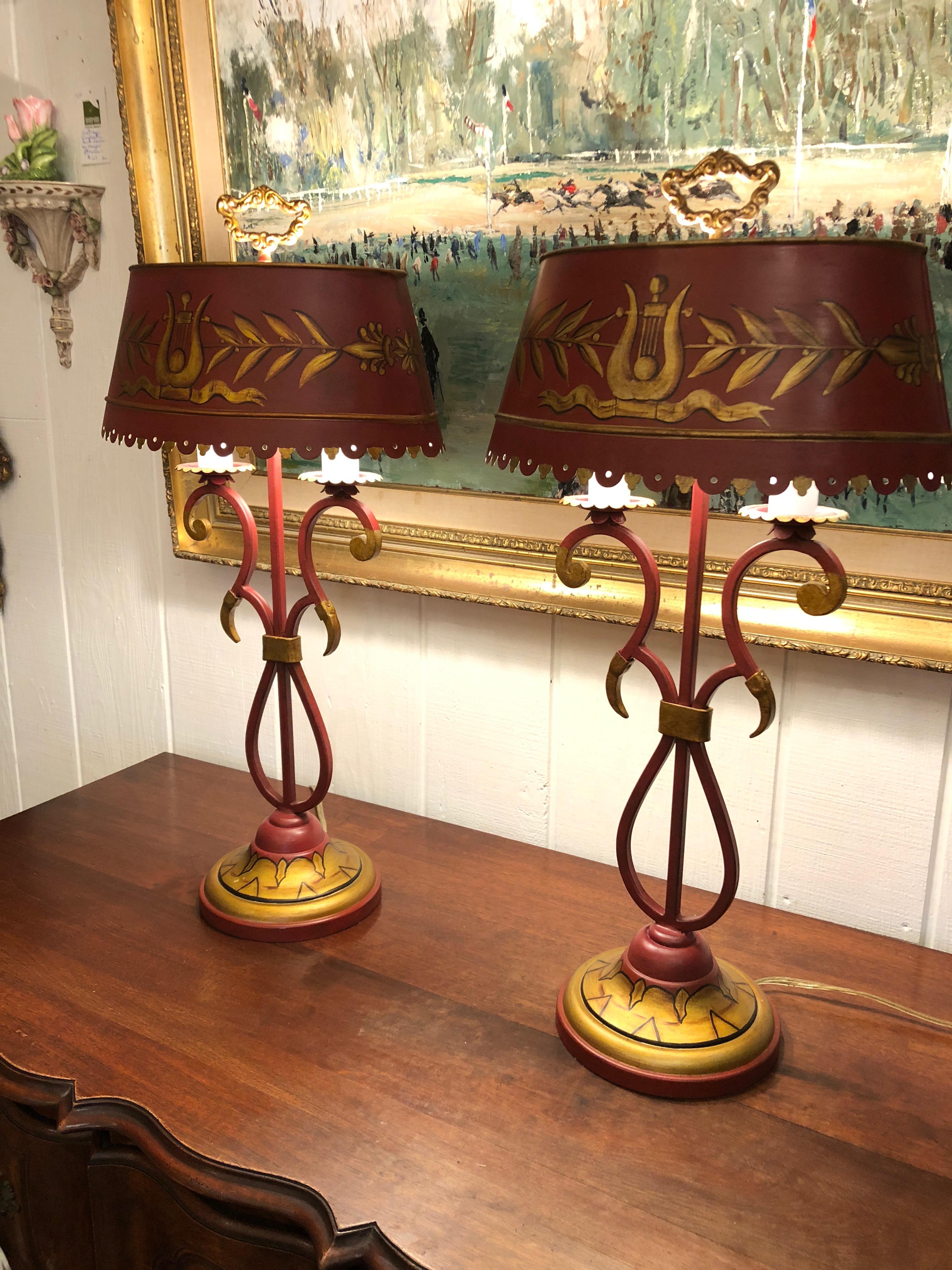 A gorgeous heavy pair of dark red tole table lamps having scalloped tin shades and gold painted lyres and neoclassical decoration. The bases are airy curlicues on painted dome shaped bases and the finial is especially ornate and lovely at the top.