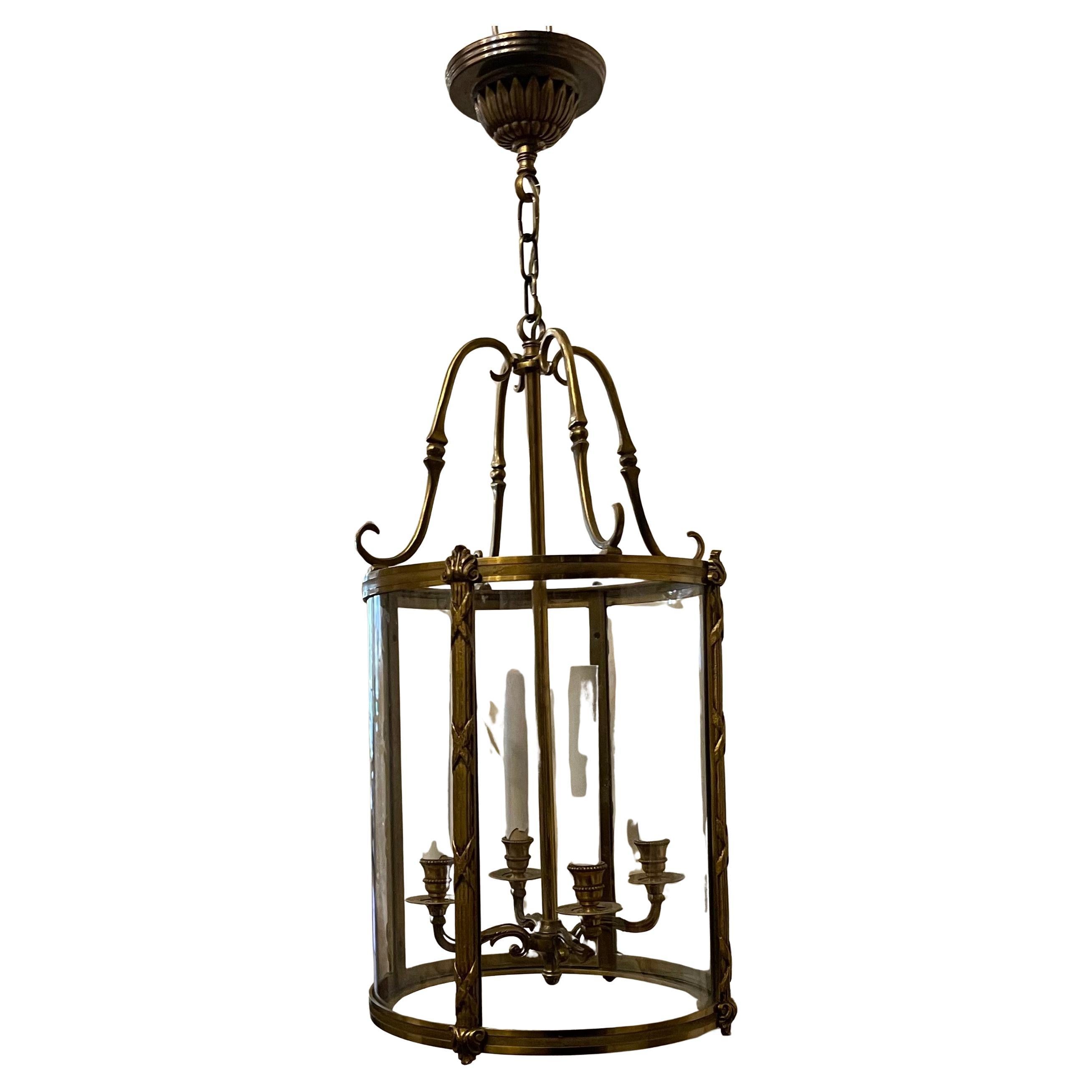 An elegant doré bronze four-light lanterns with etched ribbed bronze trim on top and bottom of the lantern are fluted reed trim around a curved glass panel. The fixture has four arms with beautiful scroll detail leading to the top crown.
