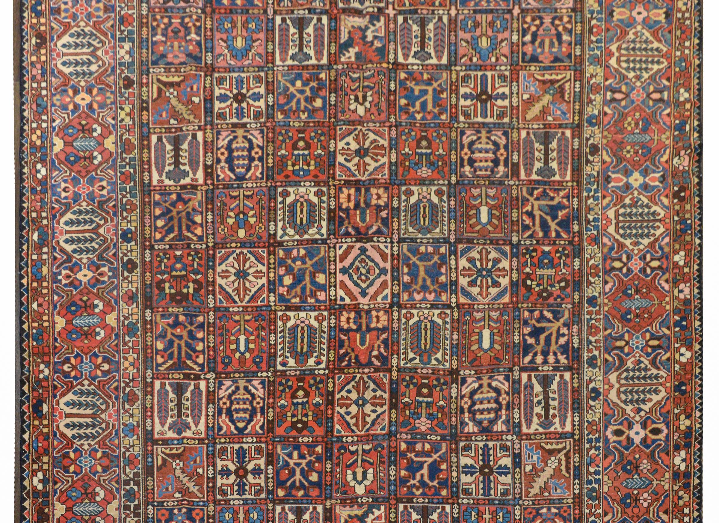 A wonderful early 20th century Persian Bakhtiari rug with a patchwork pattern of myriad stylized flowers and trees woven in crimson, light and dark indigo, green, and cream colored wool, surrounded by an extraordinary border with a large-scale