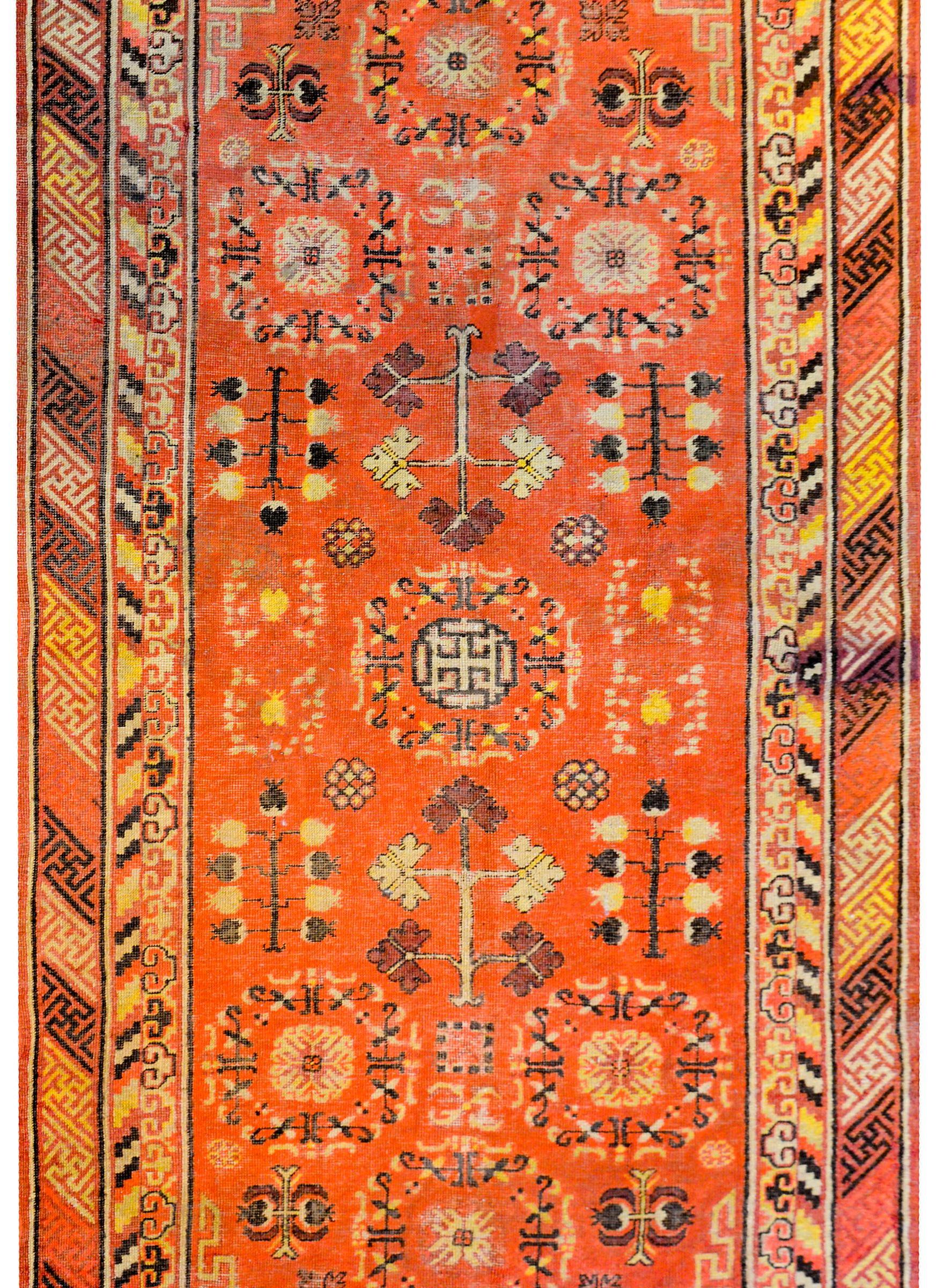 A wonderful early 20th century Central Asian Khotan rug with a beautiful central stylized floral medallion amidst a field of myriad flowers and trees-of-life on a gorgeous orange background. The border is complex with two distinct patterns, one with