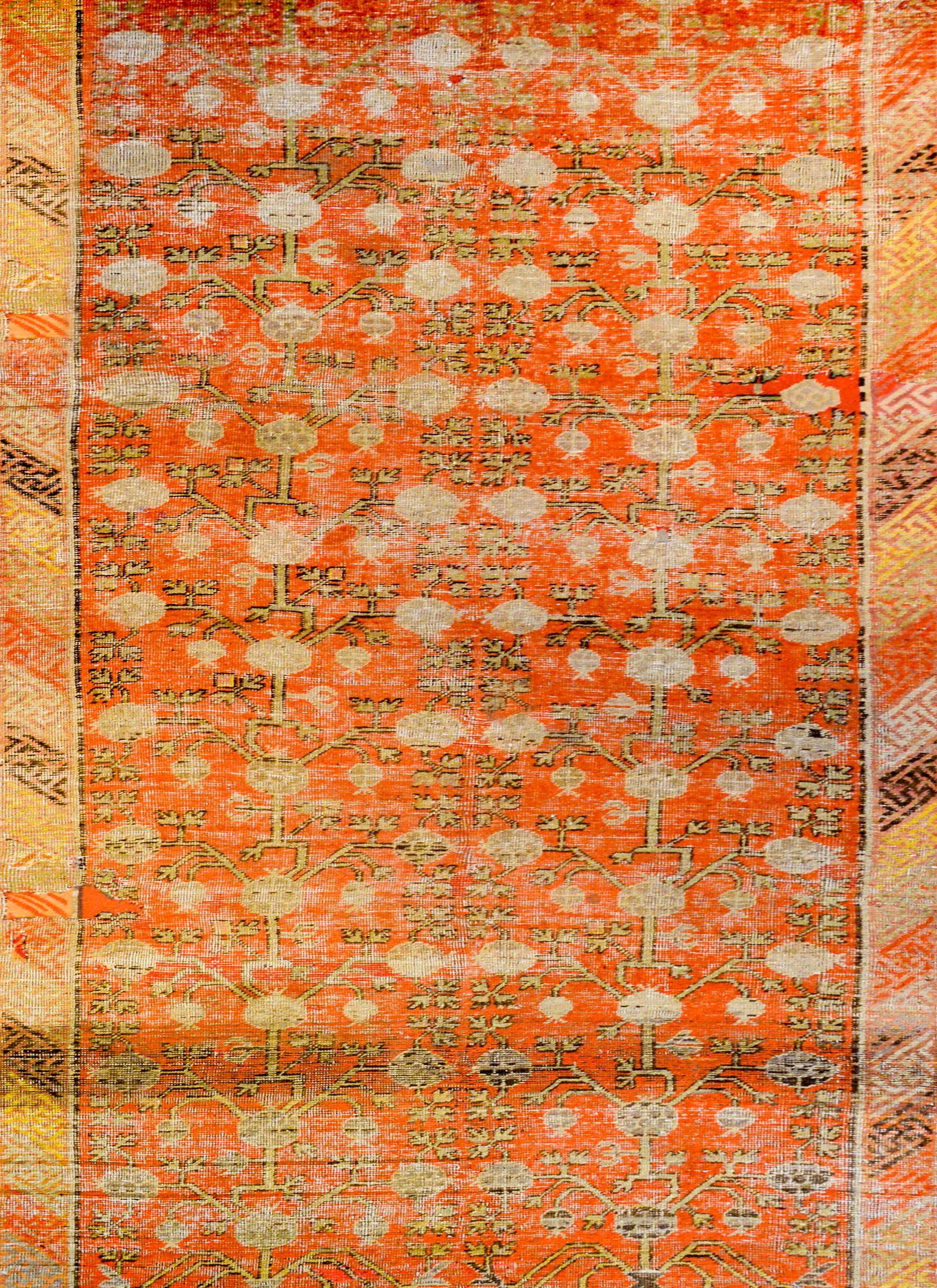 A wonderful early 20th century central Asian Khotan rug with a fantastic trellis pomegranate pattern with gold, brown, and pale indigo vegetable dyed wool on a burnt orange background. The border is beautiful comprised of an inner meandering motif