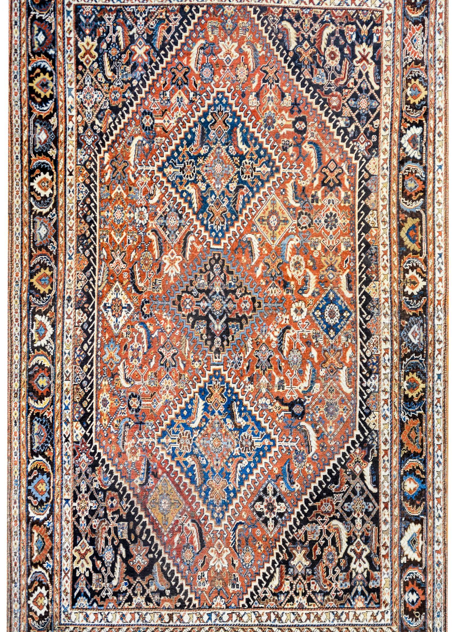 A wonderful early 20th century Persian Ghashghaei rug with three large central diamond medallions each woven with stylized floral and leaf motifs on a beautiful crimson field of flowers and leaves. The border is wide with a large-scale floral