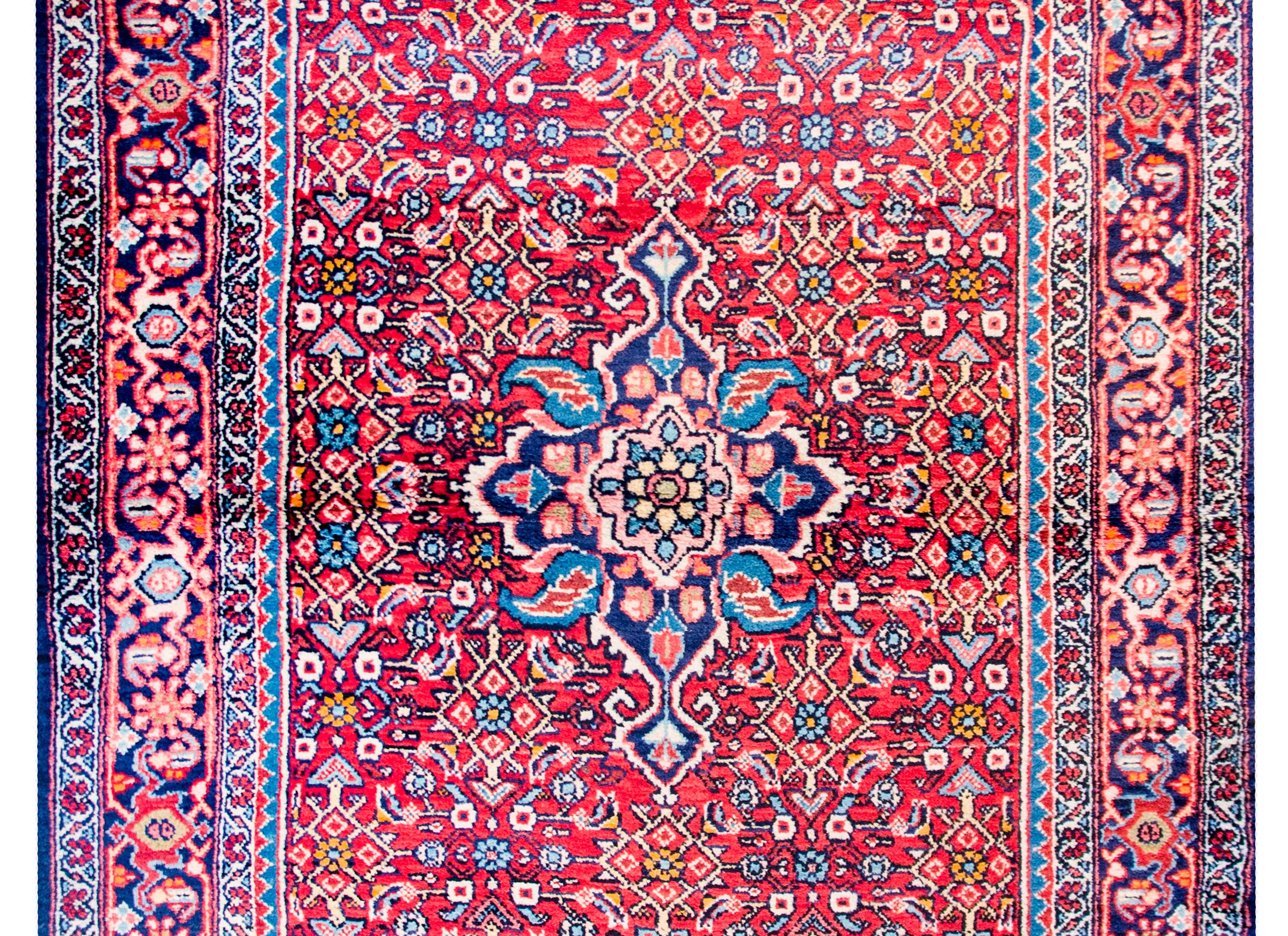 A wonderful early 20th century Persian Hamadan rug with a floral medallion woven in light and dark indigo, pink, and crimson amidst a field of flowers and trellis designs on a crimson background. The border is complex with a large-scale stylized