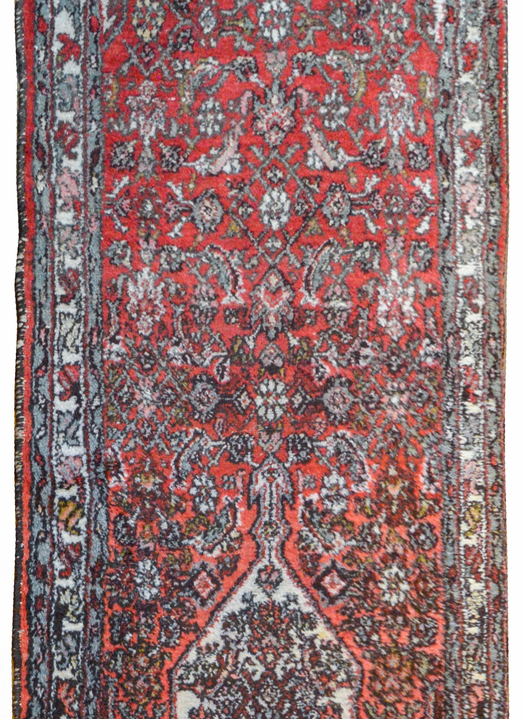 A wonderful early 20th century Hamadan runner with a large diamond medallion amidst a field of floral trellis on a coral background surrounded by a floral and leaf patterned border flanked by a pair of petite patterned floral stripes.