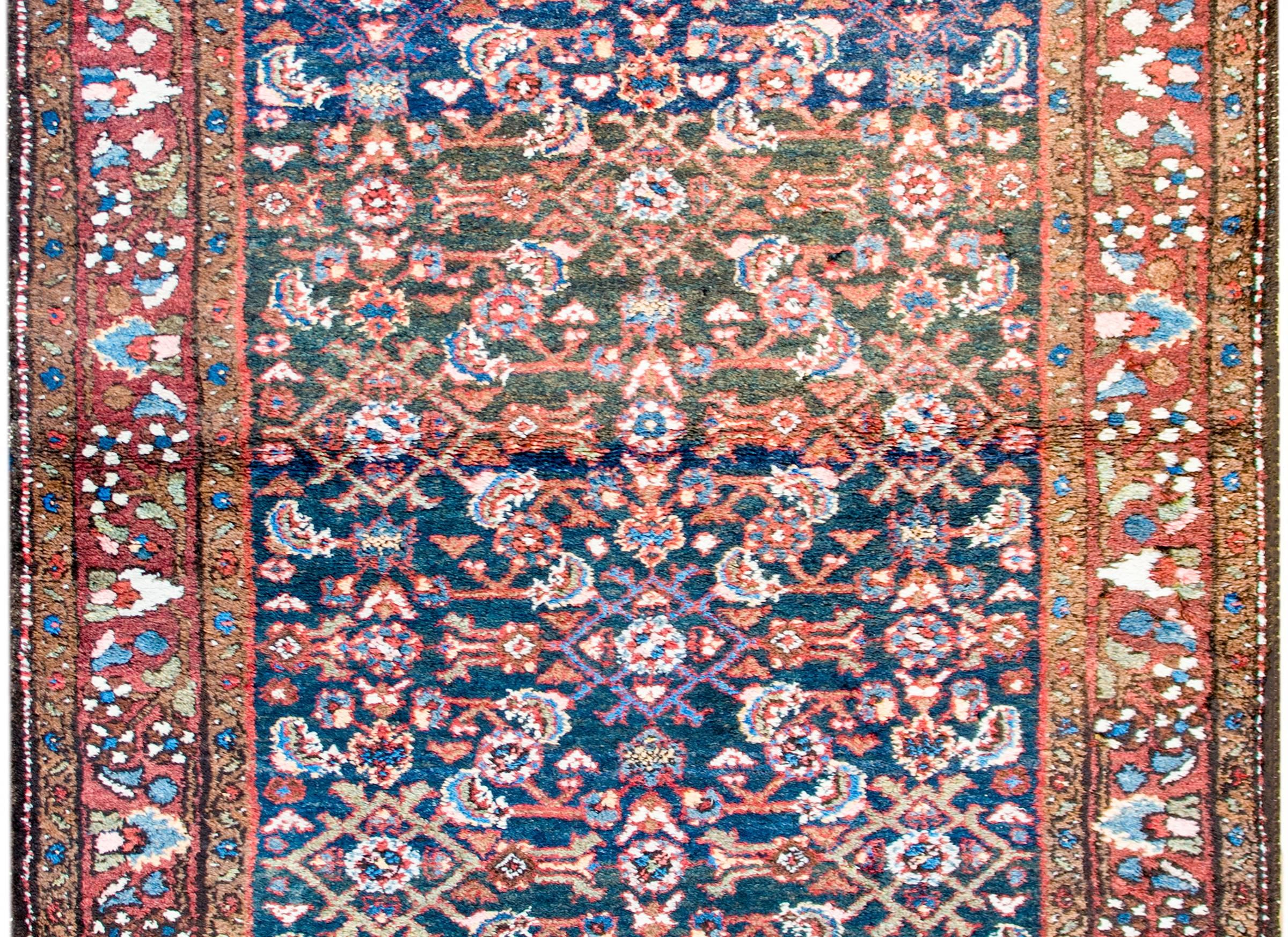 A wonderful mid-20th century Persian Herati Hamadan rug with an all-over mirrored trellis pattern of flowers and vines, woven in crimson, pink, light indigo, and white colored wool, on a dark indigo background. The border is complex with a
