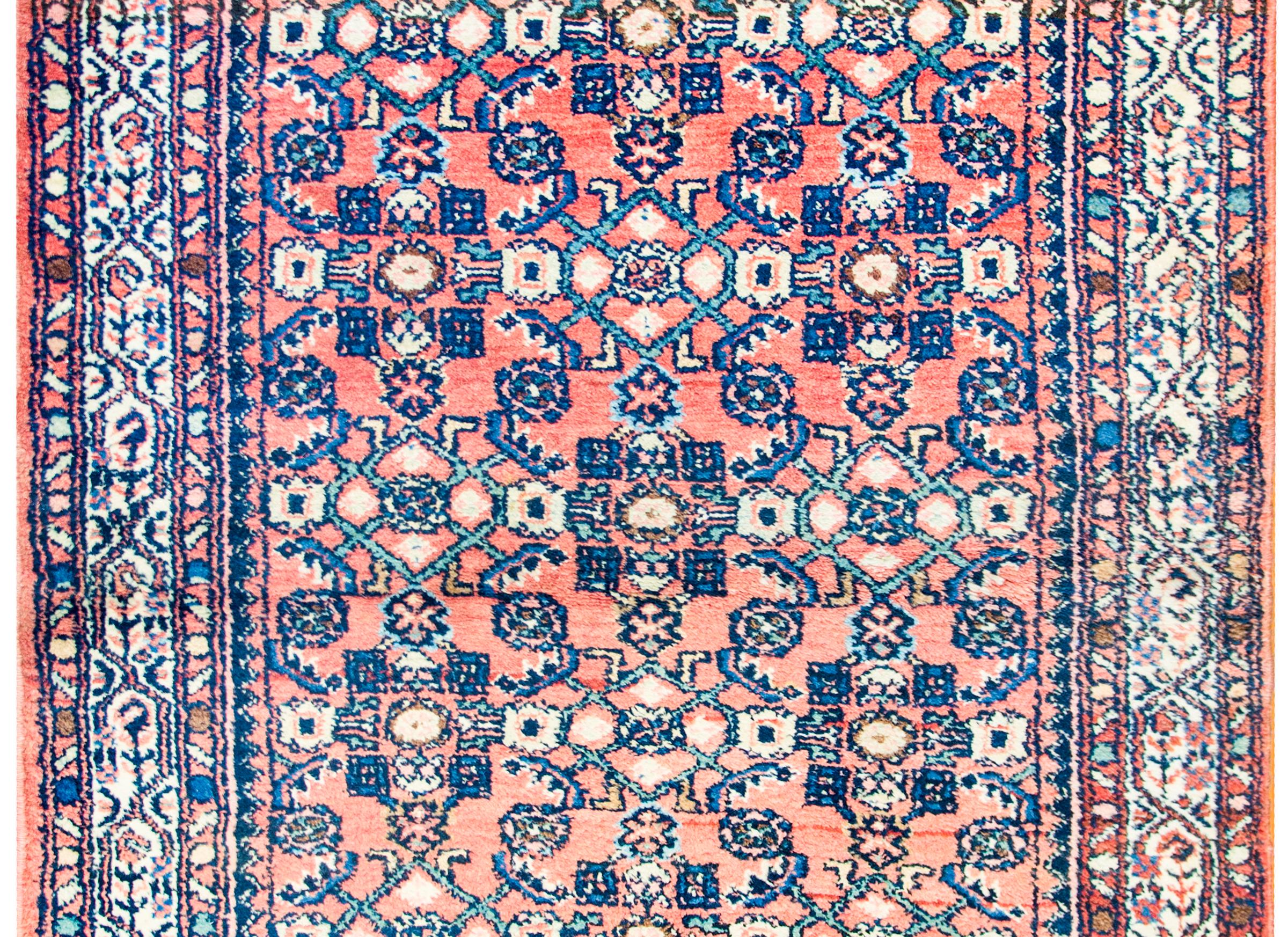 Early 20th century Persian Herati rug with a fantastic trellis and stylized floral pattern woven in indigo and cream colored wool, in an abrash crimson background surrounded by a border with a stylized floral patterned central stripe flanked by two