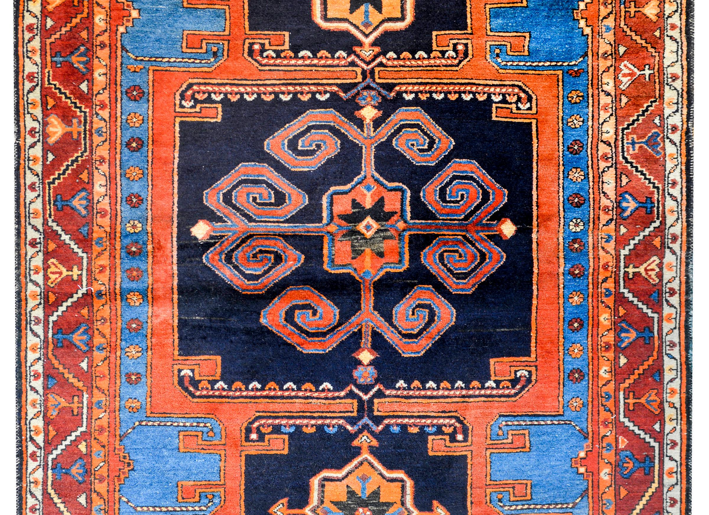 A wonderful early 20th century Persian Karabab rug with a bold tribal pattern containing a large central stylized floral medallion woven in light indigo and crimson on a dark indigo background amidst a field of multiple stylized flowers and