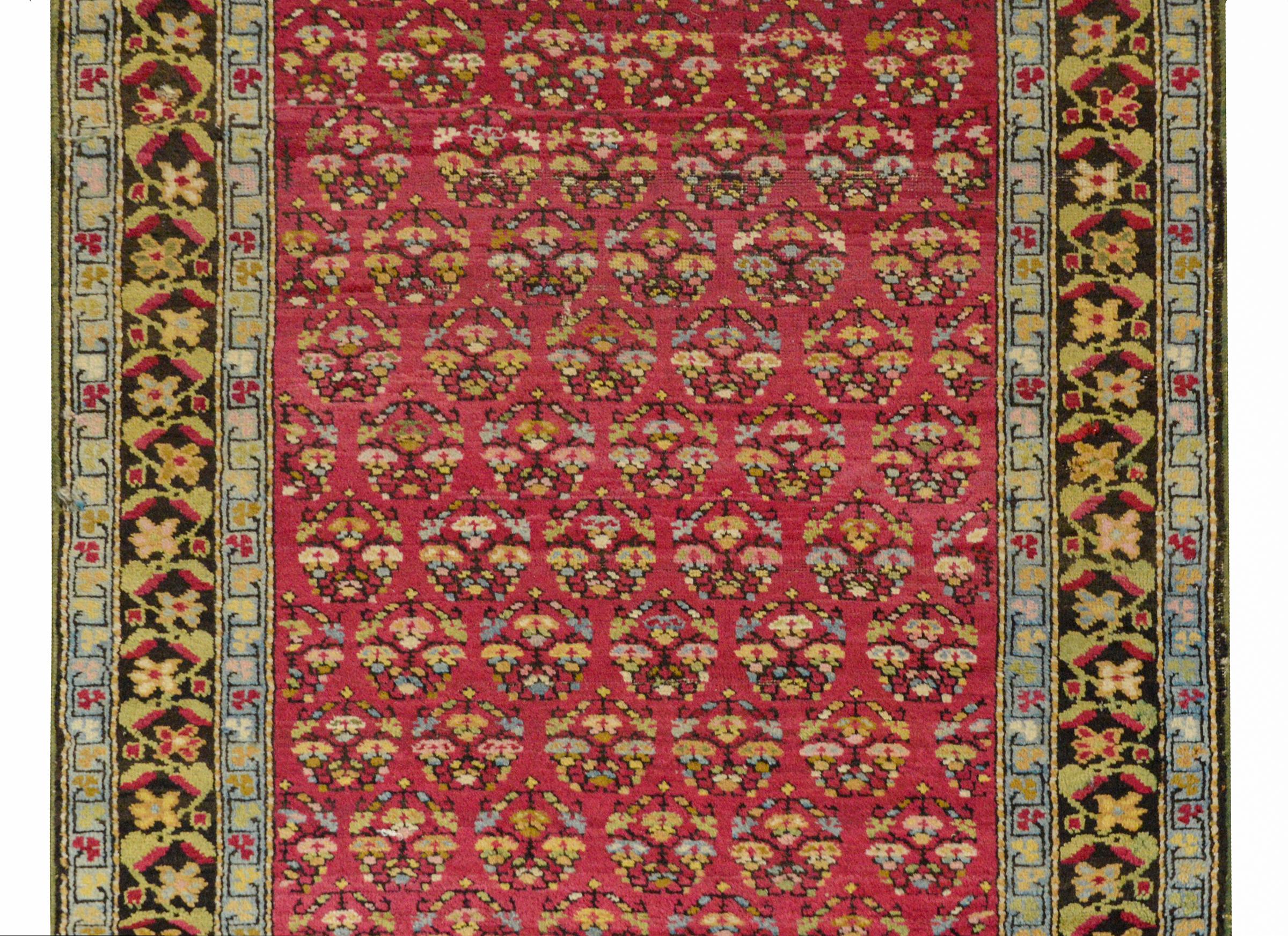 A wonderful early 20th century Karabakh runner with an all-over tree-of-life floral pattern woven in pink, gold, green, and pale indigo on a dark fuchsia background. The border is beautiful with a stylized pink and green floral and vine pattern