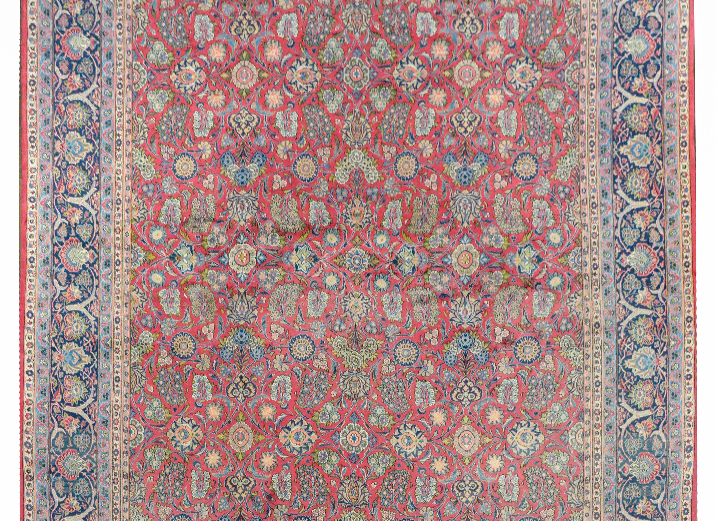 A wonderful early 20th century Persian Kashan Dabir rug with a fantastic all-over mirrored pattern containing myriad flower varieties woven in light and dark indigo, cream, dark and light green, orange, and pink, all on a cranberry background. The